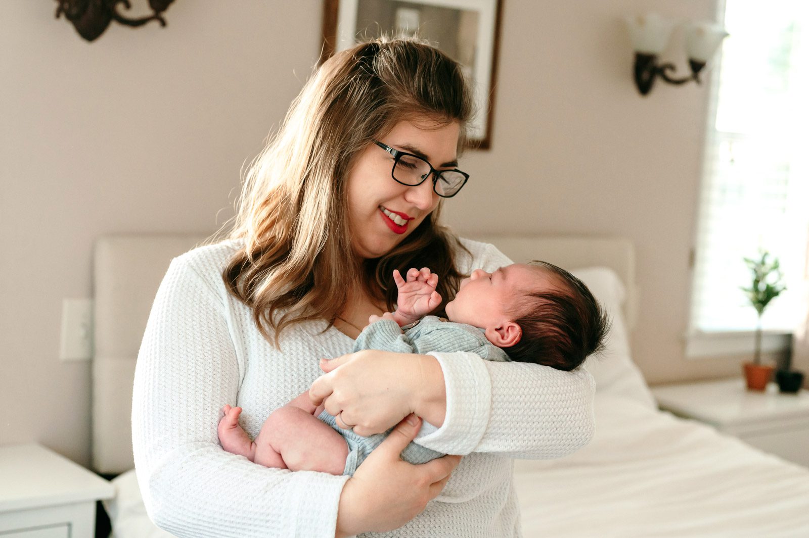 a new mother cradling her baby boy in her arms and smiling down at him during an in home newborn photo session
