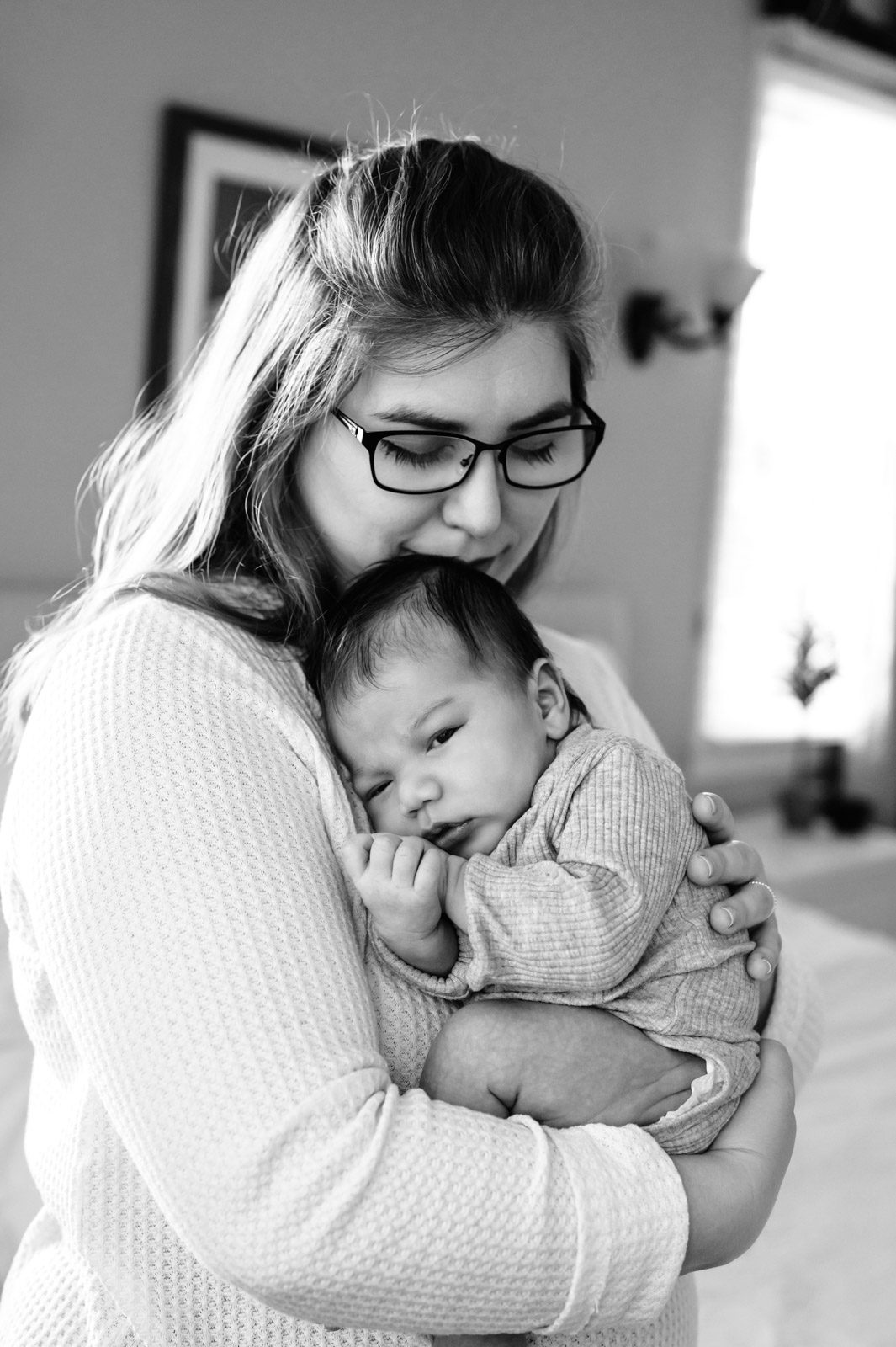 a black and white picture of a new mom snuggling her newborn baby boy against her chest during a newborn photoshoot