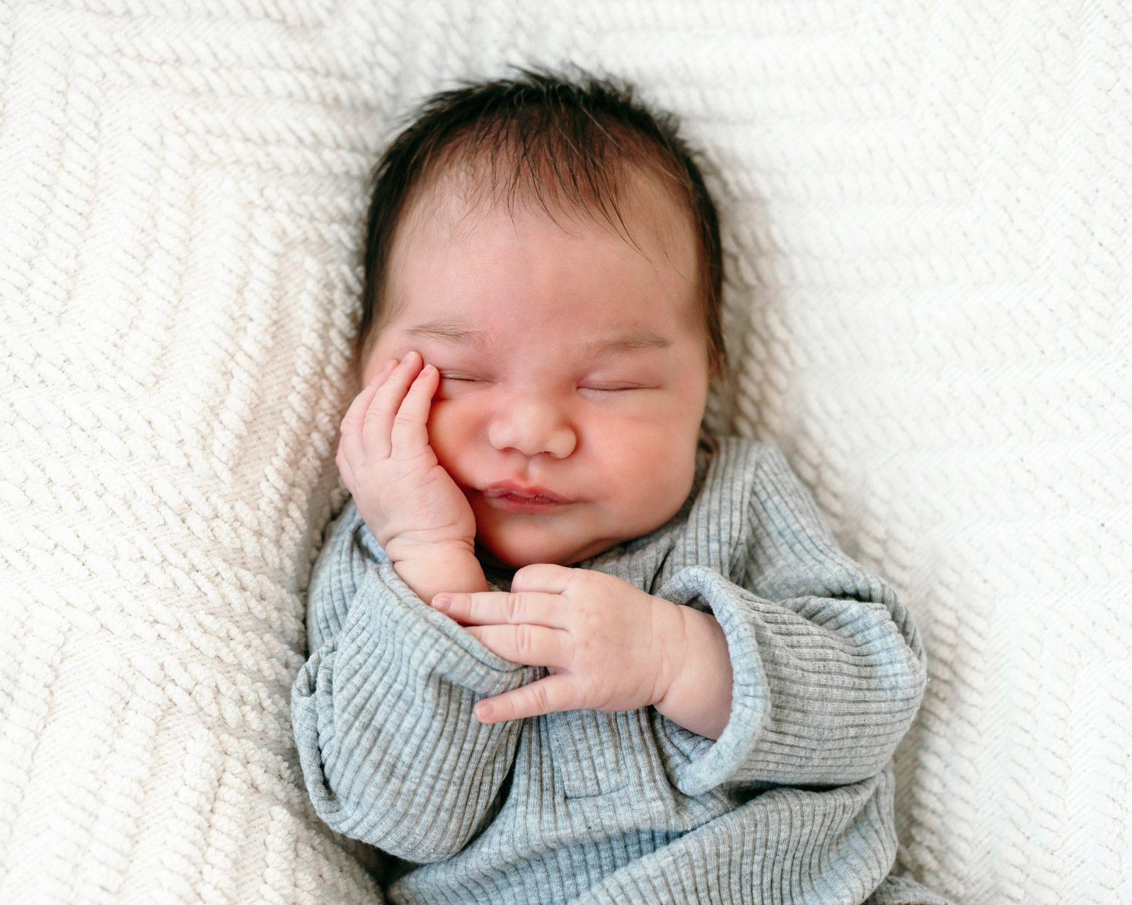 a baby boy holding hand hand against his cheek during a newborn photoshoot