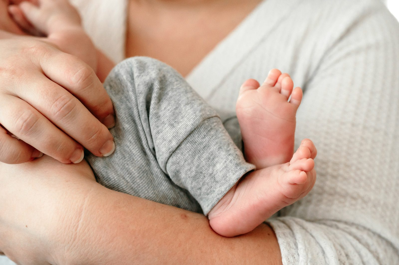a close up picture of a newborn baby boy's feet while his mother cradles him in her arms during an in home newborn photoshoot