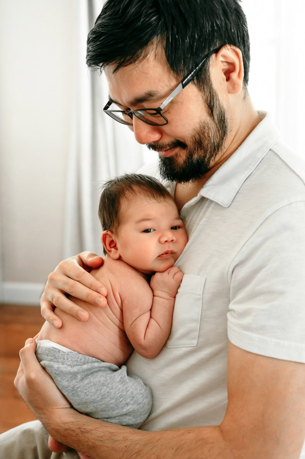 a new father cradling his newborn baby boy against his chest during an in home photoshoot