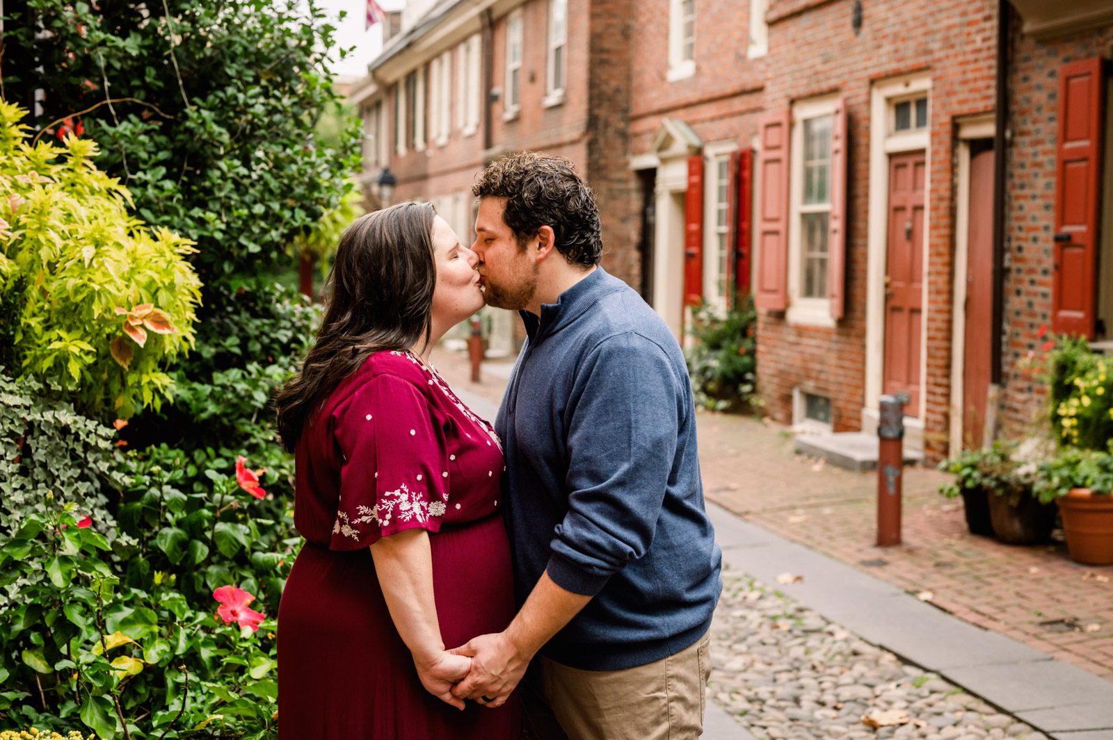 expecting parents holding hands and kissing in Elfreth's Alley during a Philadelphia maternity photoshoot