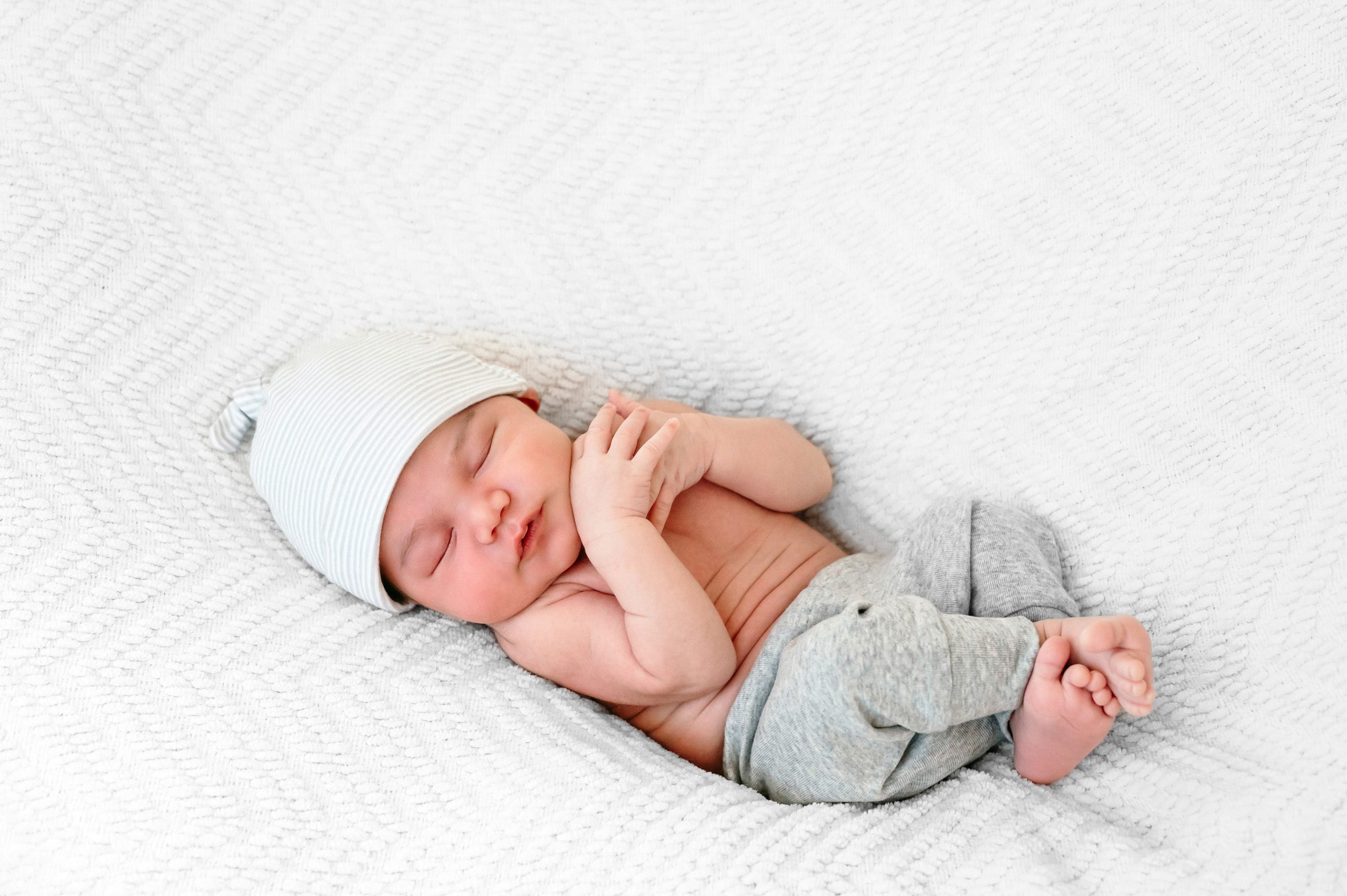a newborn baby boy sleeping with his arms and legs tucked in close to his body during an in home newborn photoshoot