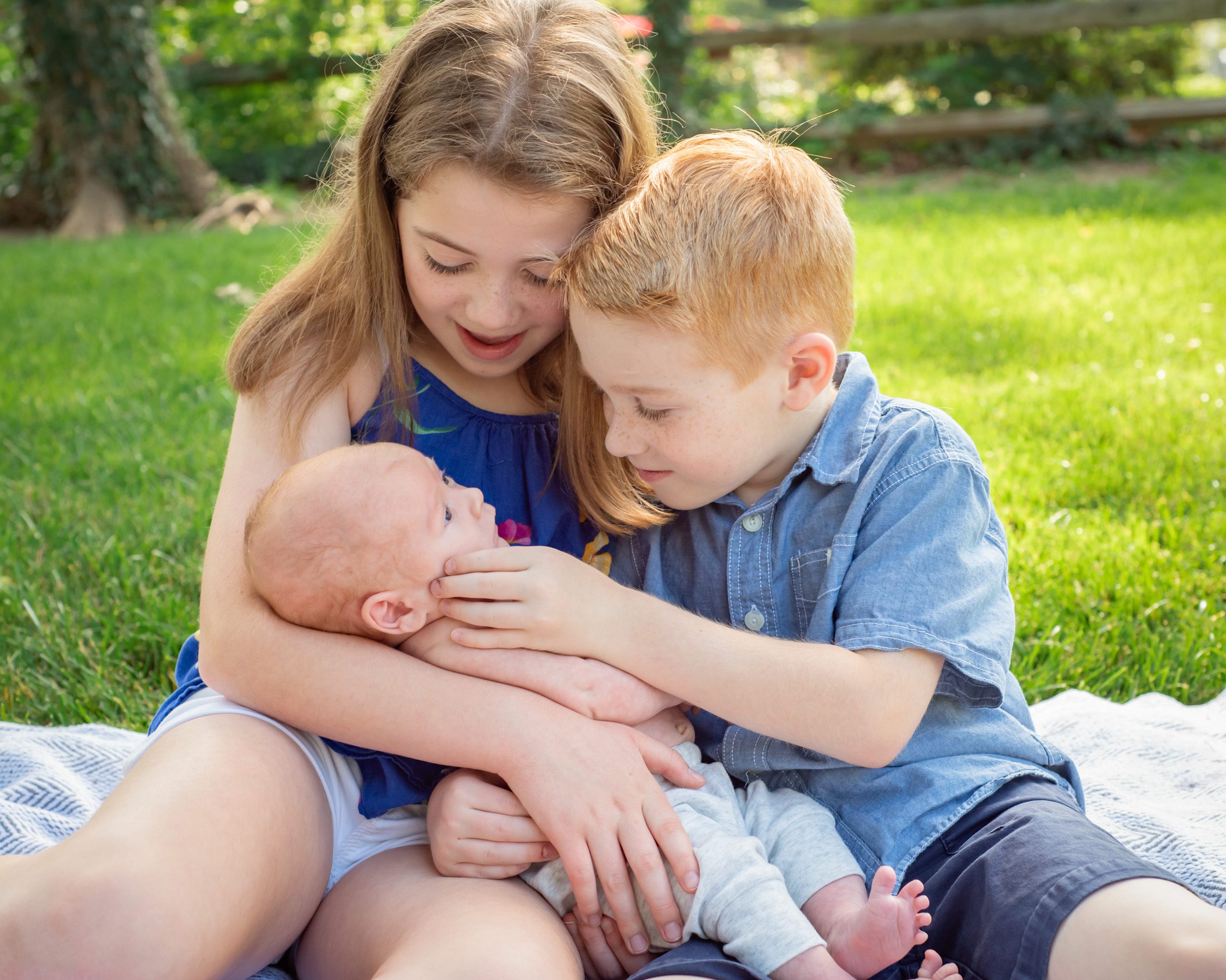 Newborn photo of two older siblings holding their baby brother and touching his cheek during a Pottstown family photoshoot