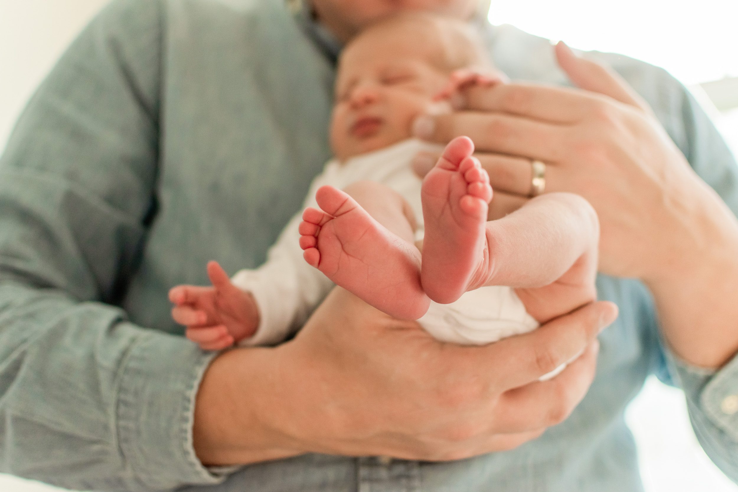 Close up photo of newborn boy's feet while dad holds him in his arms during an in home newborn photo session