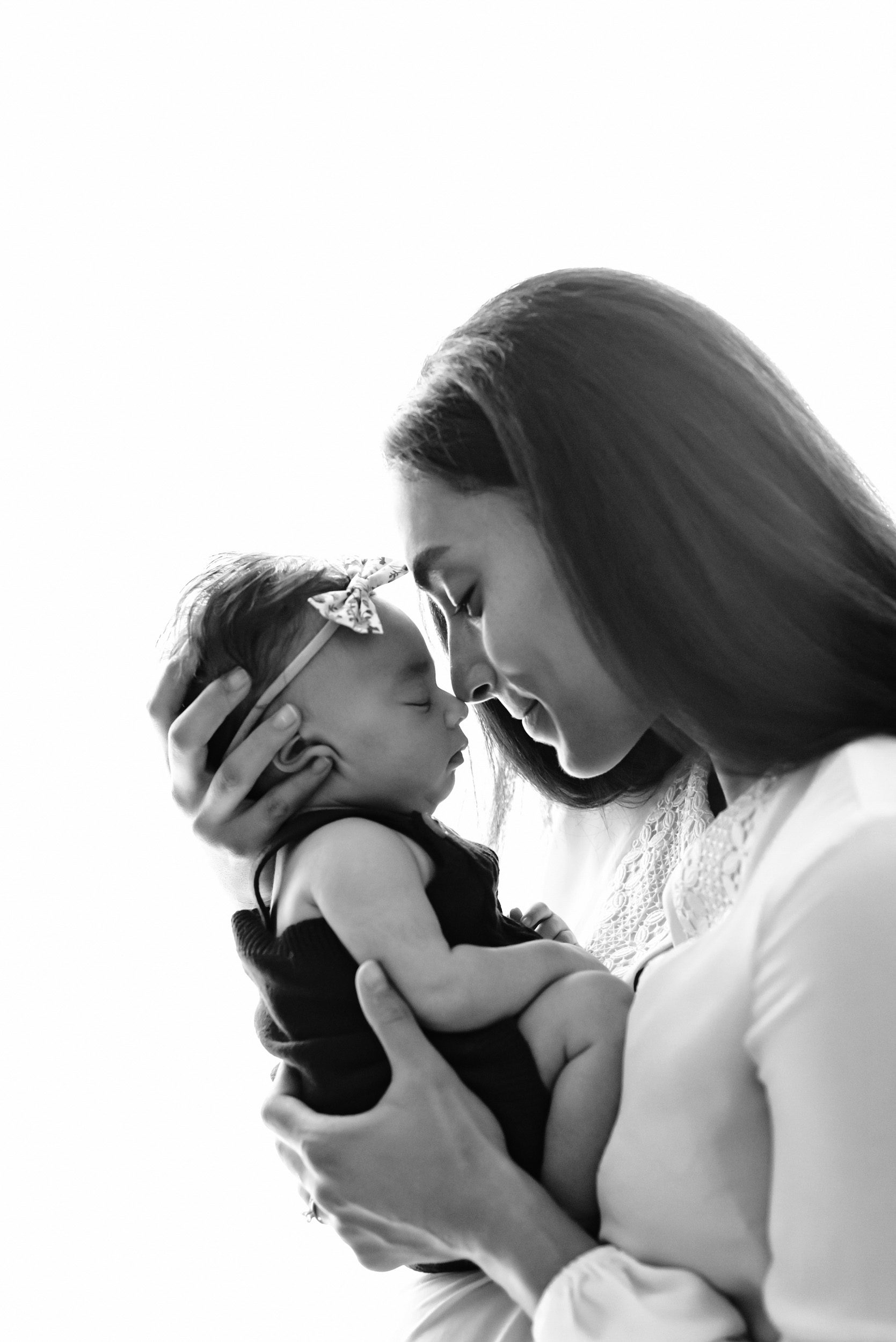 Black and white photo of a mom nuzzling noses with her newborn baby girl during an in home newborn photography session