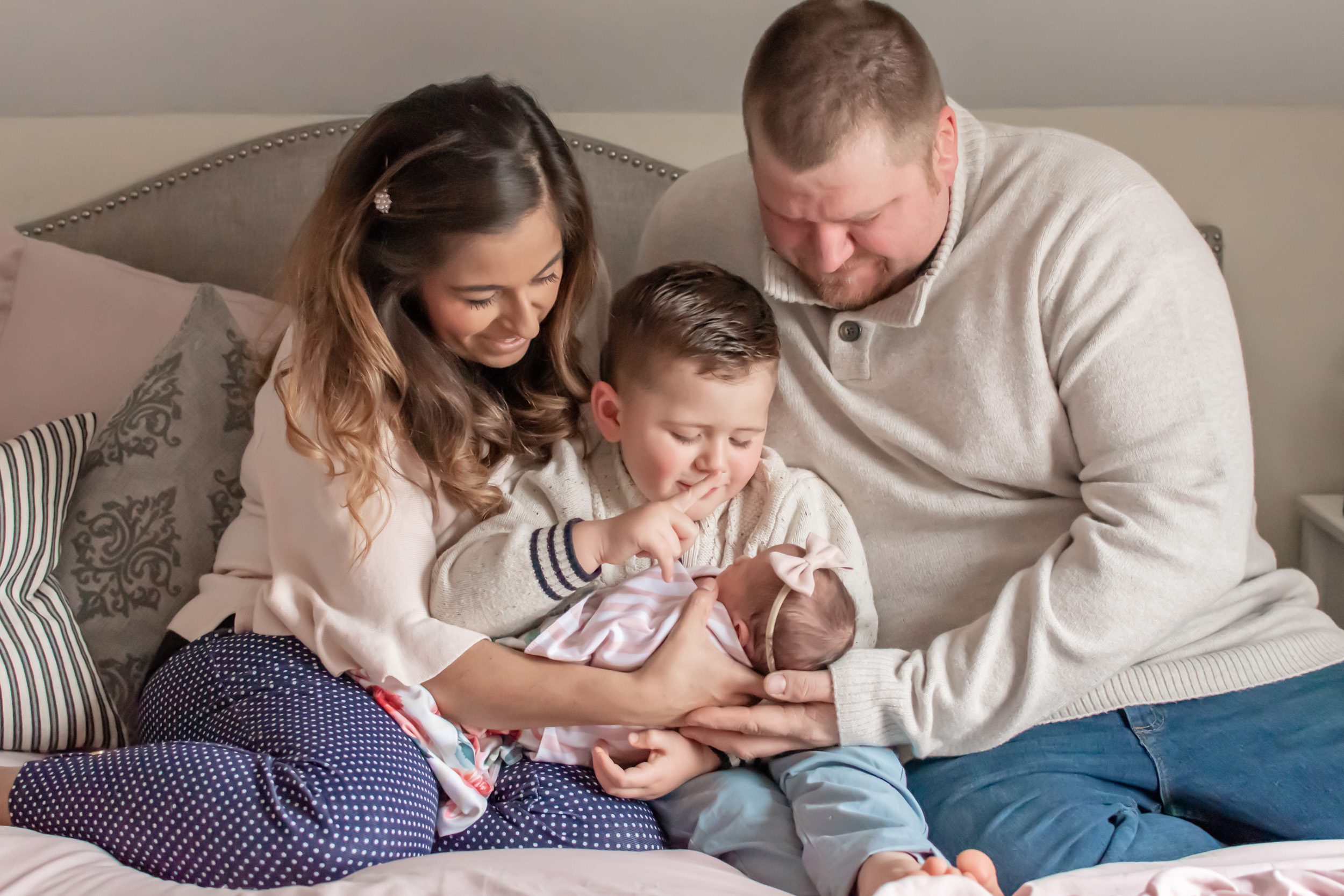 Newborn picture of older brother on his parents' lap holding his baby sister and comforting her during an in home newborn photography session