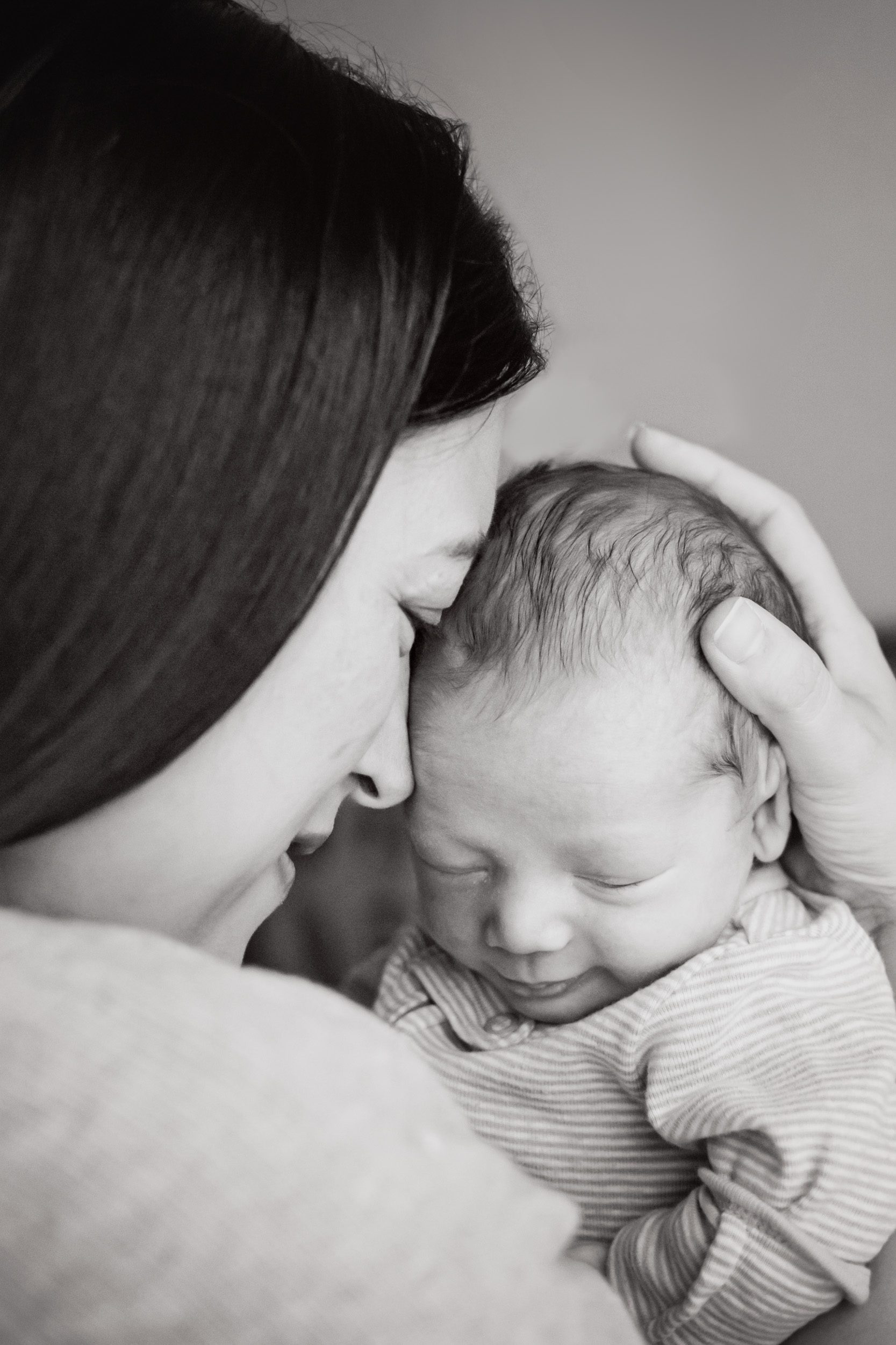 Black and white picture of a mom resting her forehead against her newborn son during an in home newborn photography session