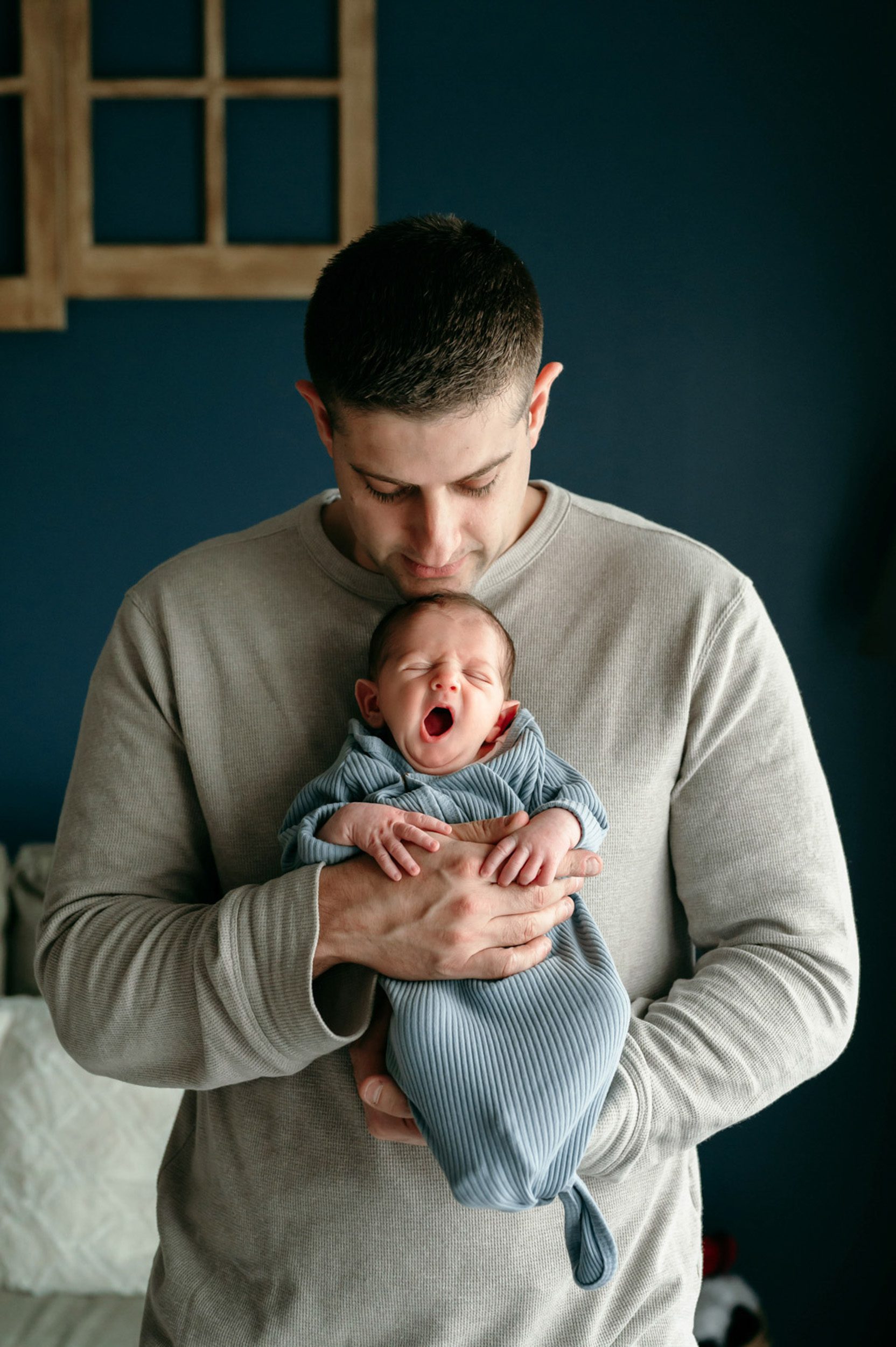 Newborn photo of a baby boy yawning while his dad holds him against his chest during a natural newborn photo session