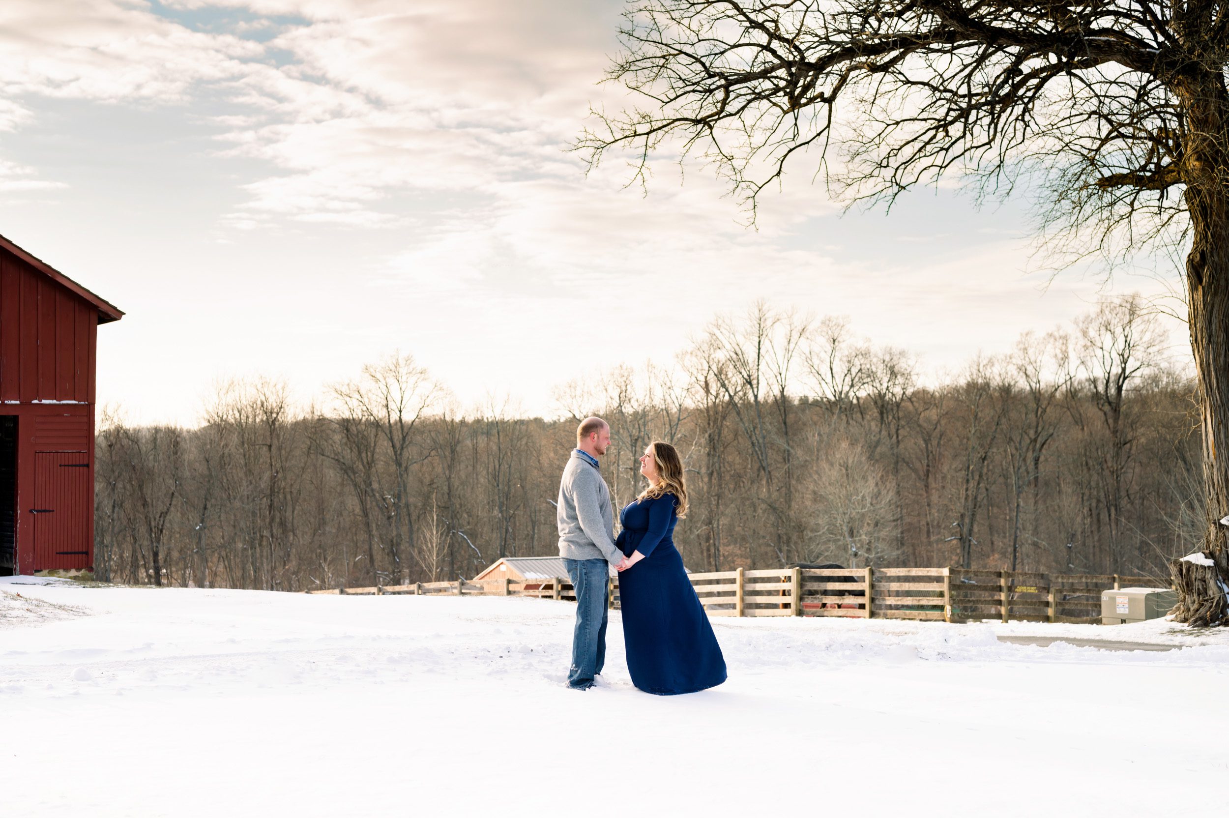 expecting couple holding hands and smiling at each other in a snowy field at a sunset maternity session