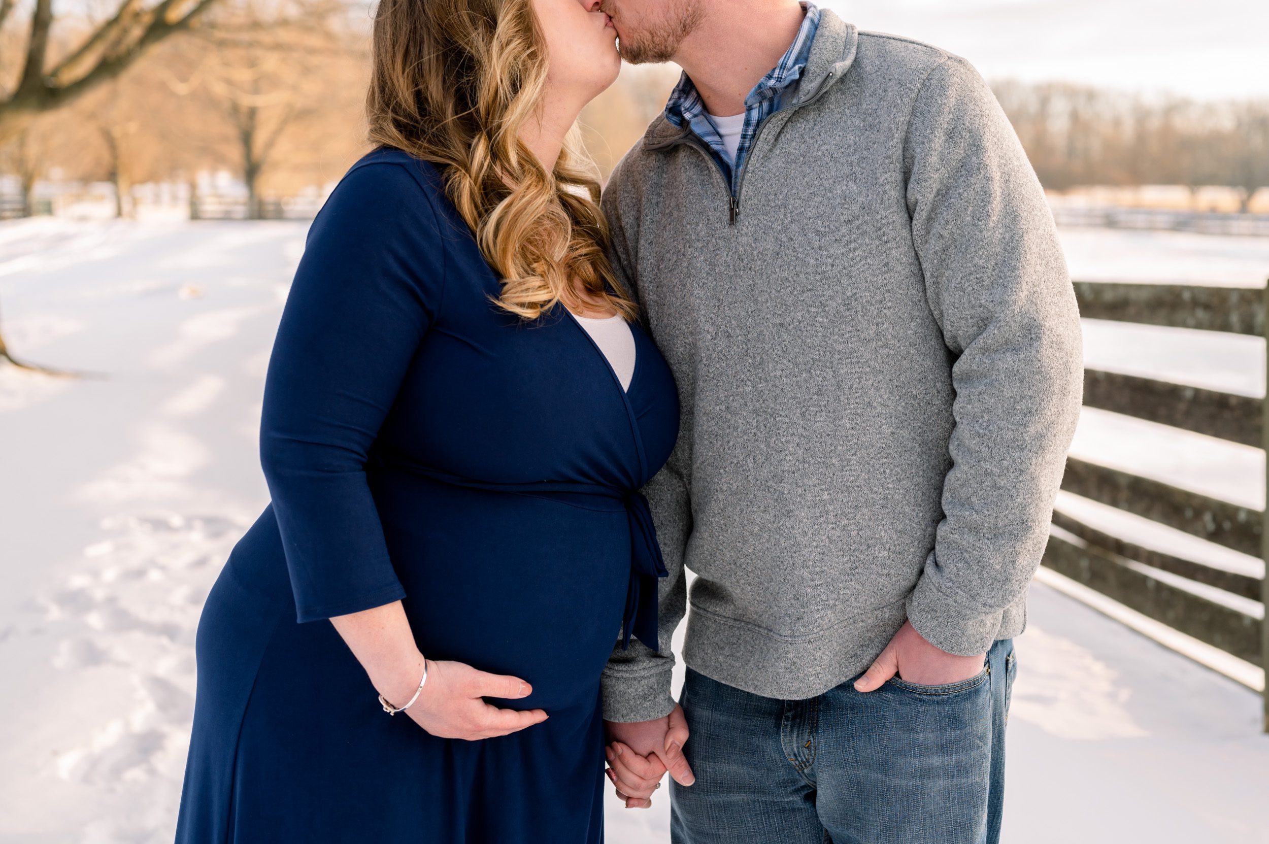 Close up picture of expecting parents holding hands and kissing in the snow at a maternity photo session