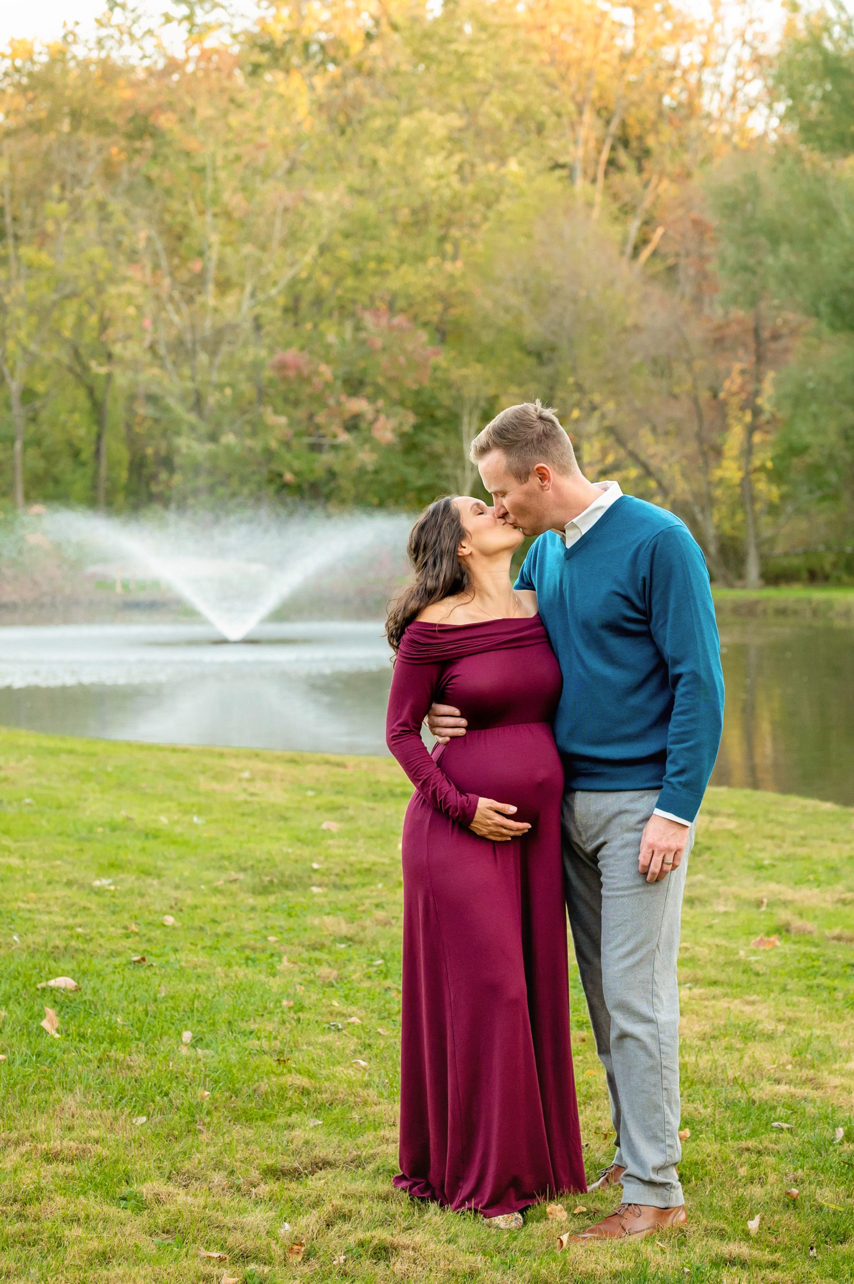 an expecting couple kissing in front of a fountain as the mom cradles her belly during a Phoenixville maternity photoshoot 