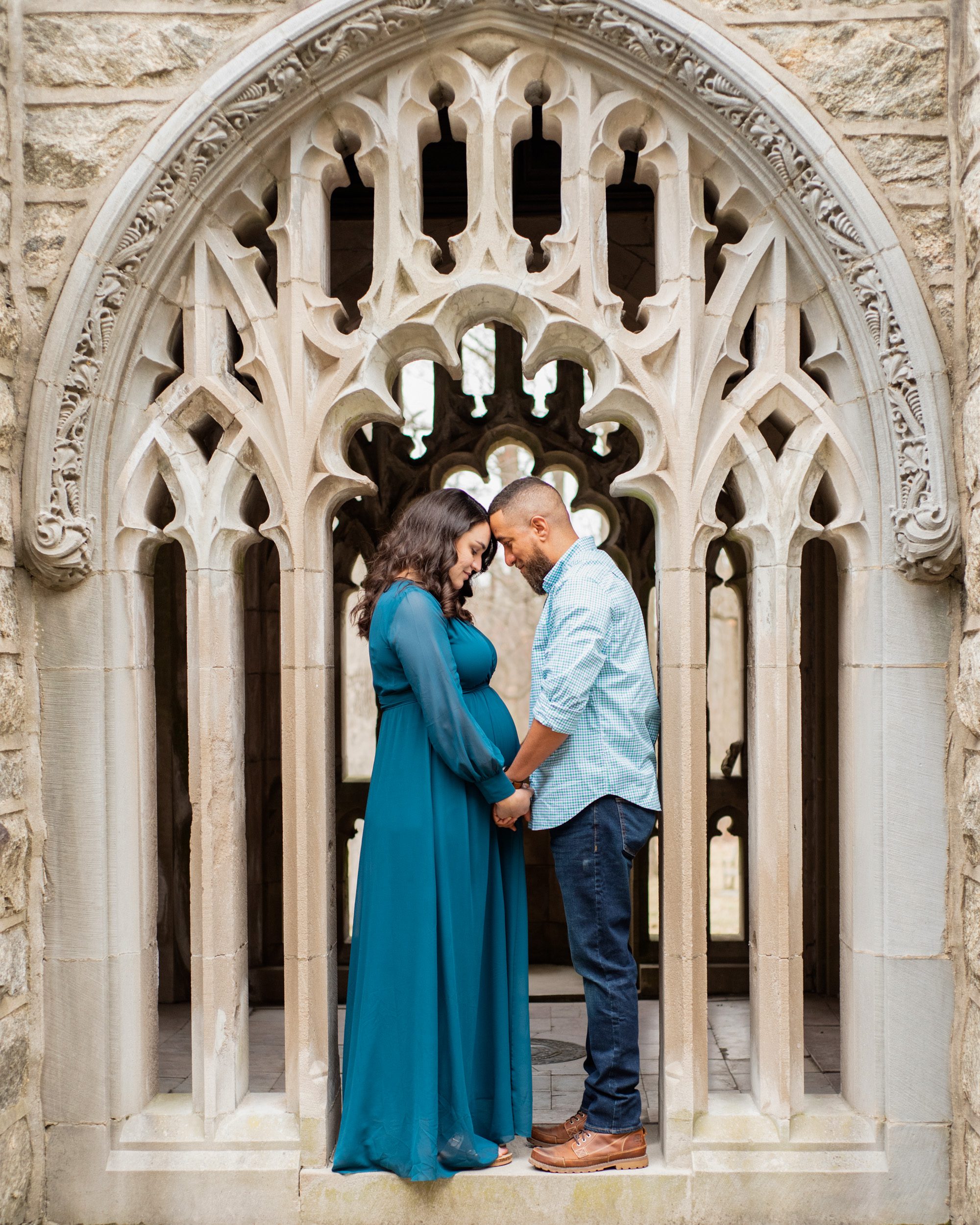 expecting parents resting their foreheads together and holding hands under a stone archway at a maternity photoshoot