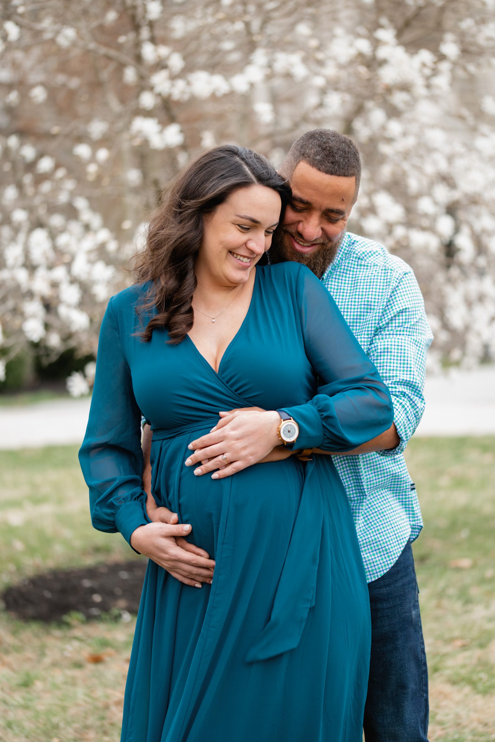 expecting mother in a blue  dress laughing while dad hugs her from behind at a maternity photoshoot