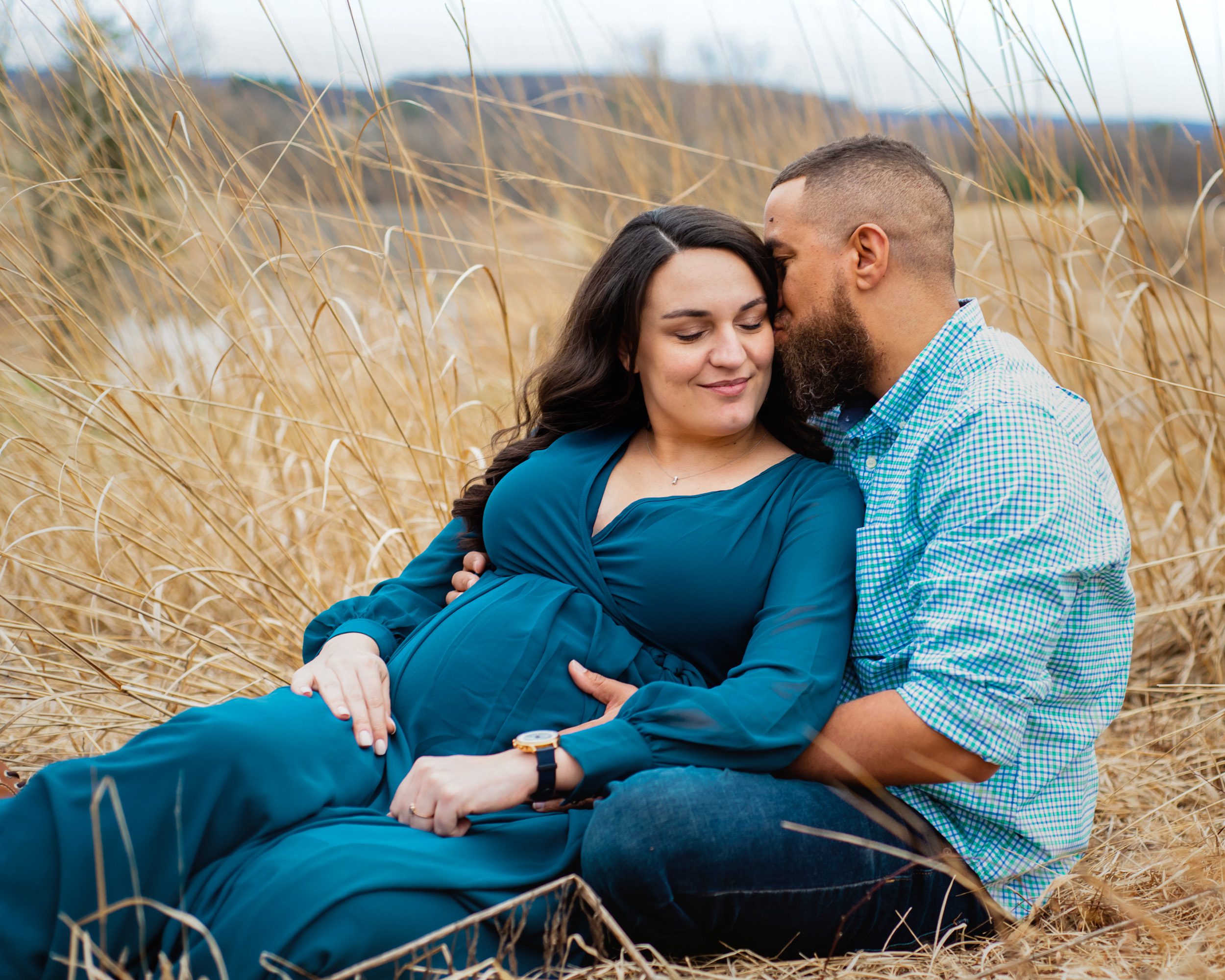 expecting parents sitting and snuggling in a field of golden grasses at a maternity photoshoot