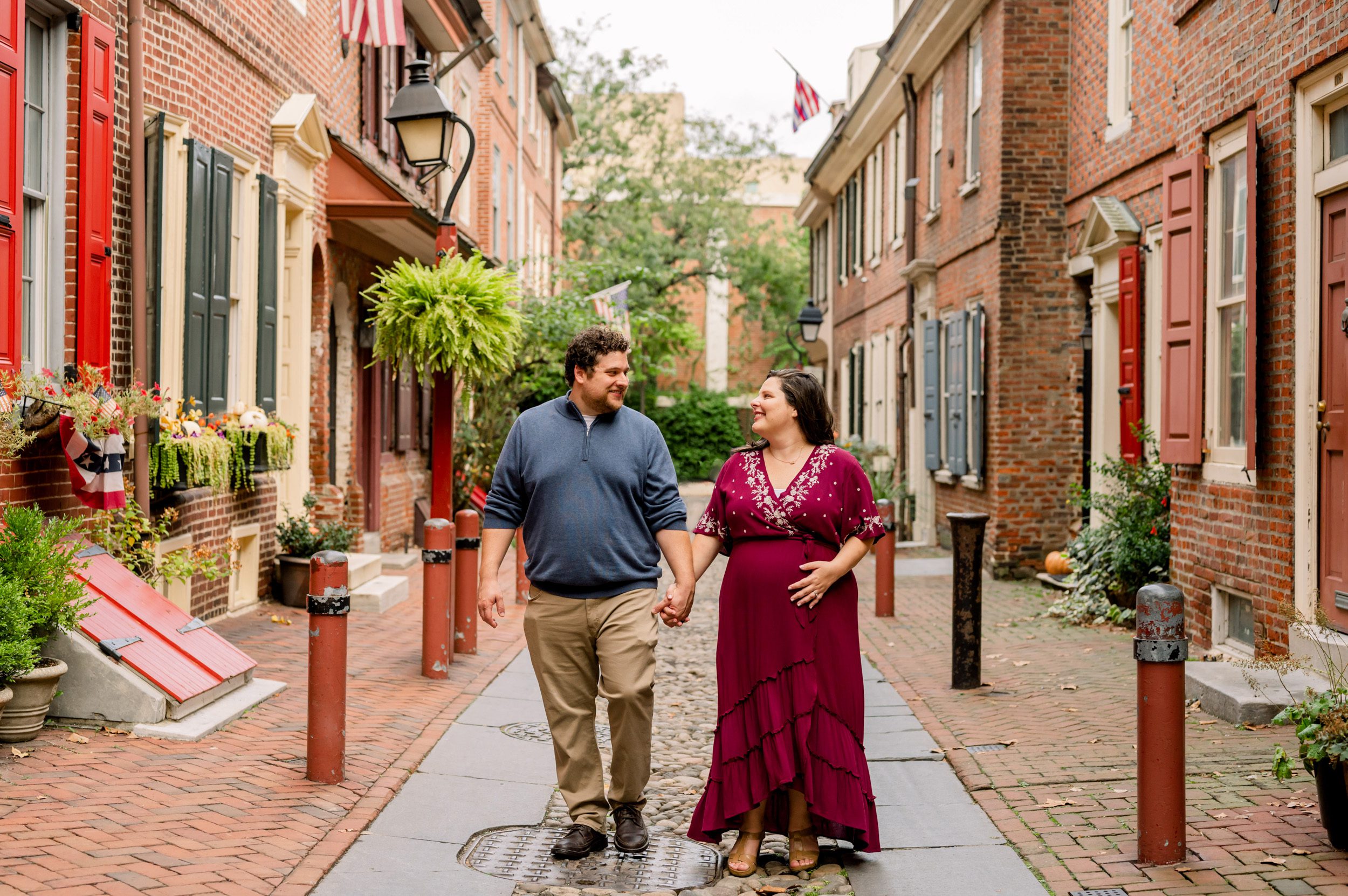 expecting parents walking down a city alley holding hands and smiling at each other during a Philadelphia maternity photo session