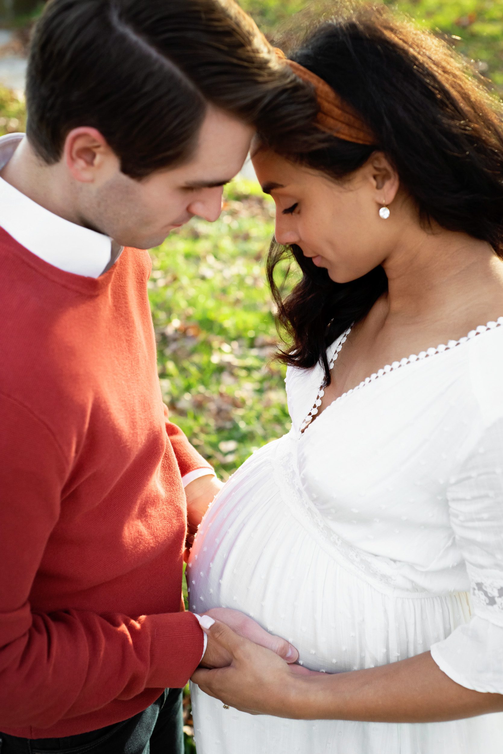 expecting parents resting their foreheads together and looking down at mom's belly at a maternity photoshoot
