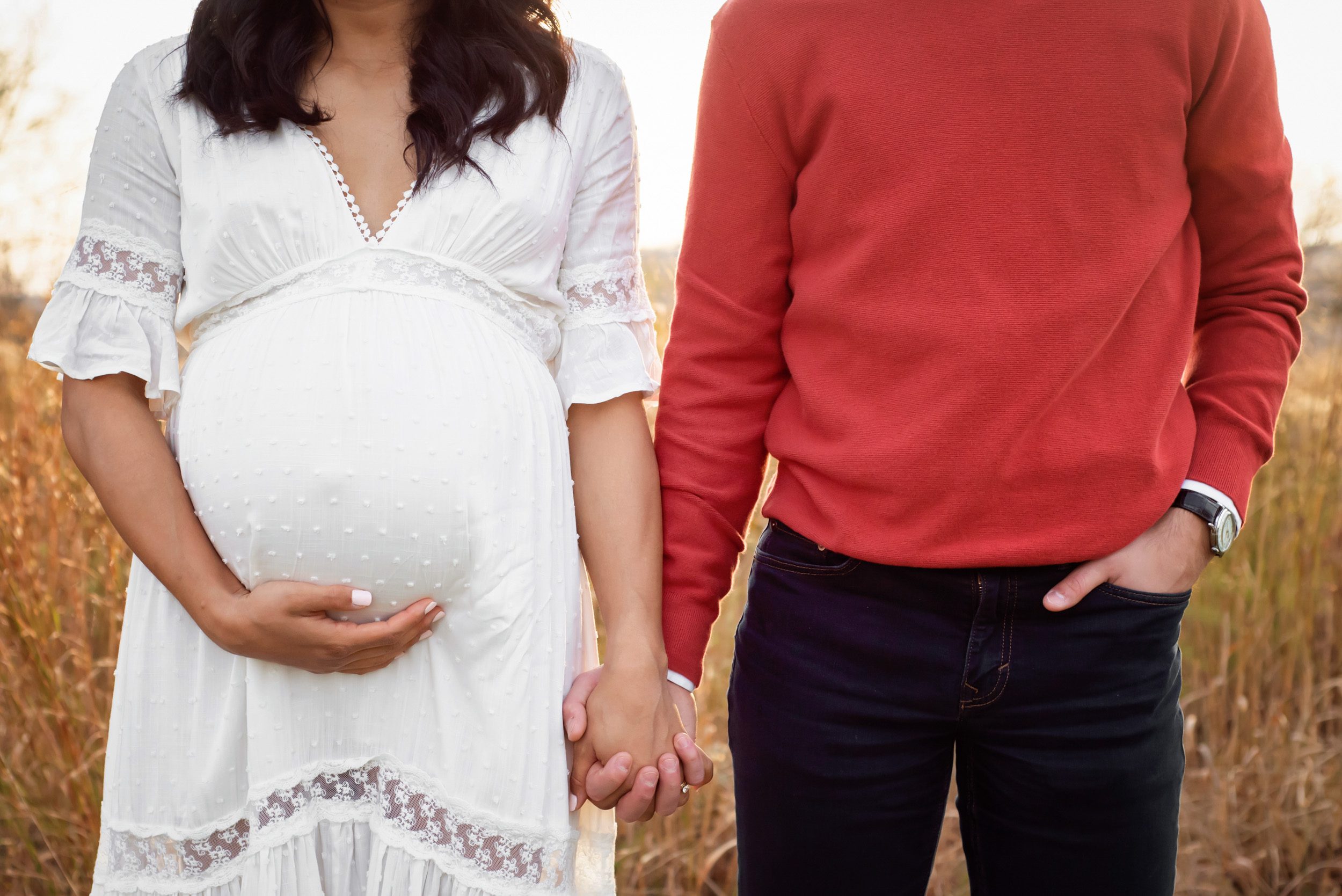 a close up of an expecting mom's belly with dad standing next to her and holding her hand during a winter maternity photoshoot