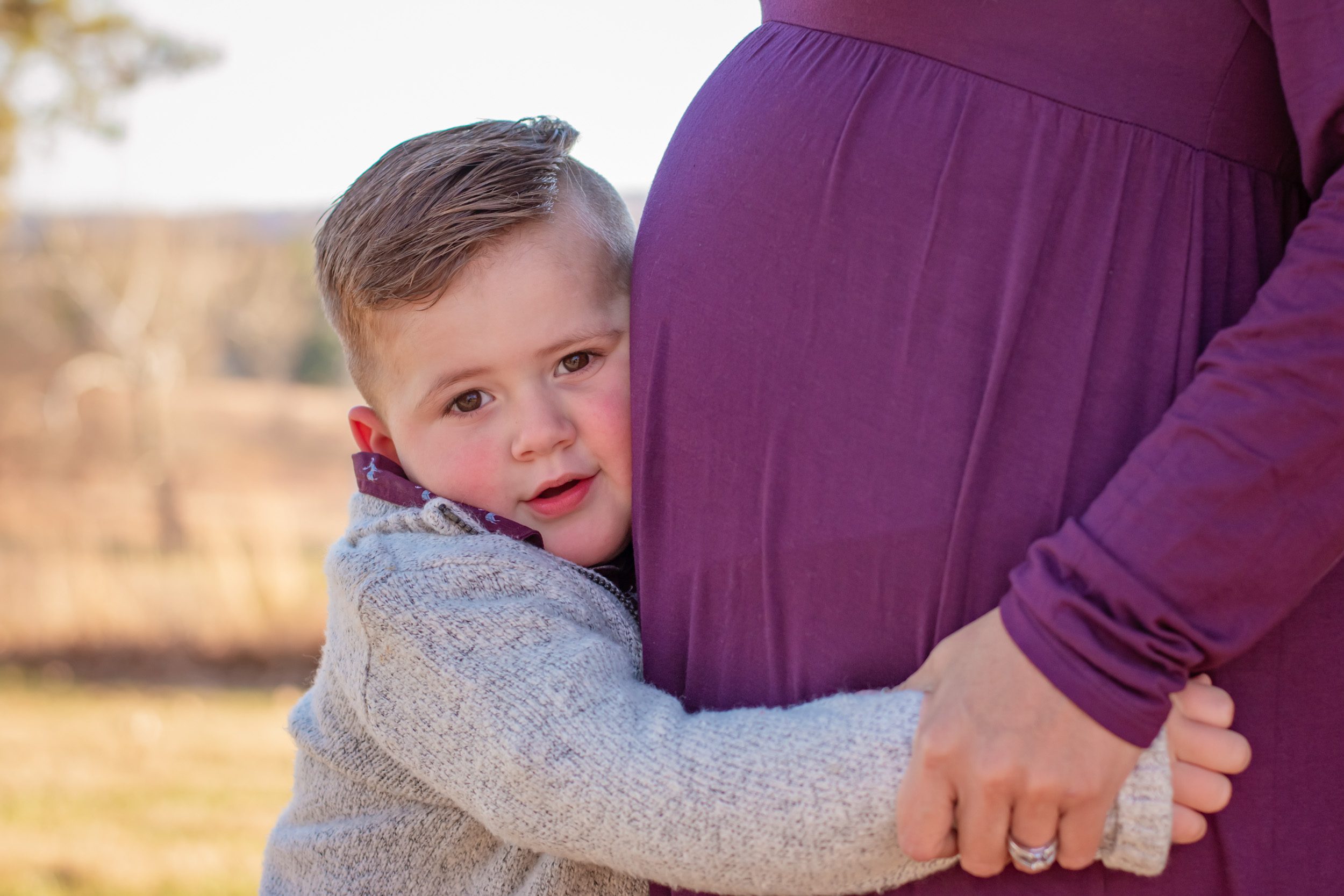 Close up picture of a young boy hugging his expecting mom's belly at a maternity photoshoot