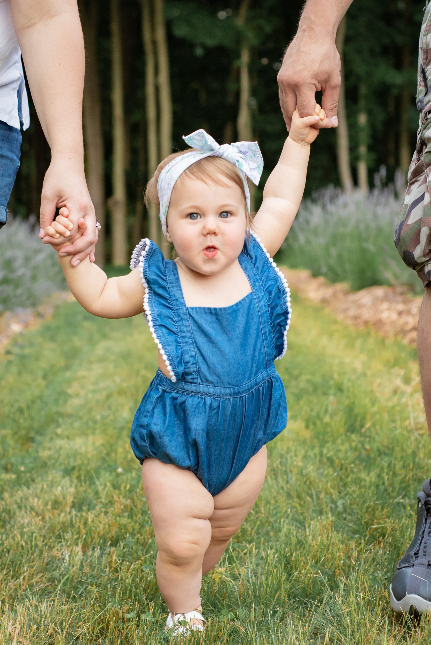Close up picture of a little girl making a surprised face as she walks through a lavender field holding her mom and dad's hands during a family photoshoot