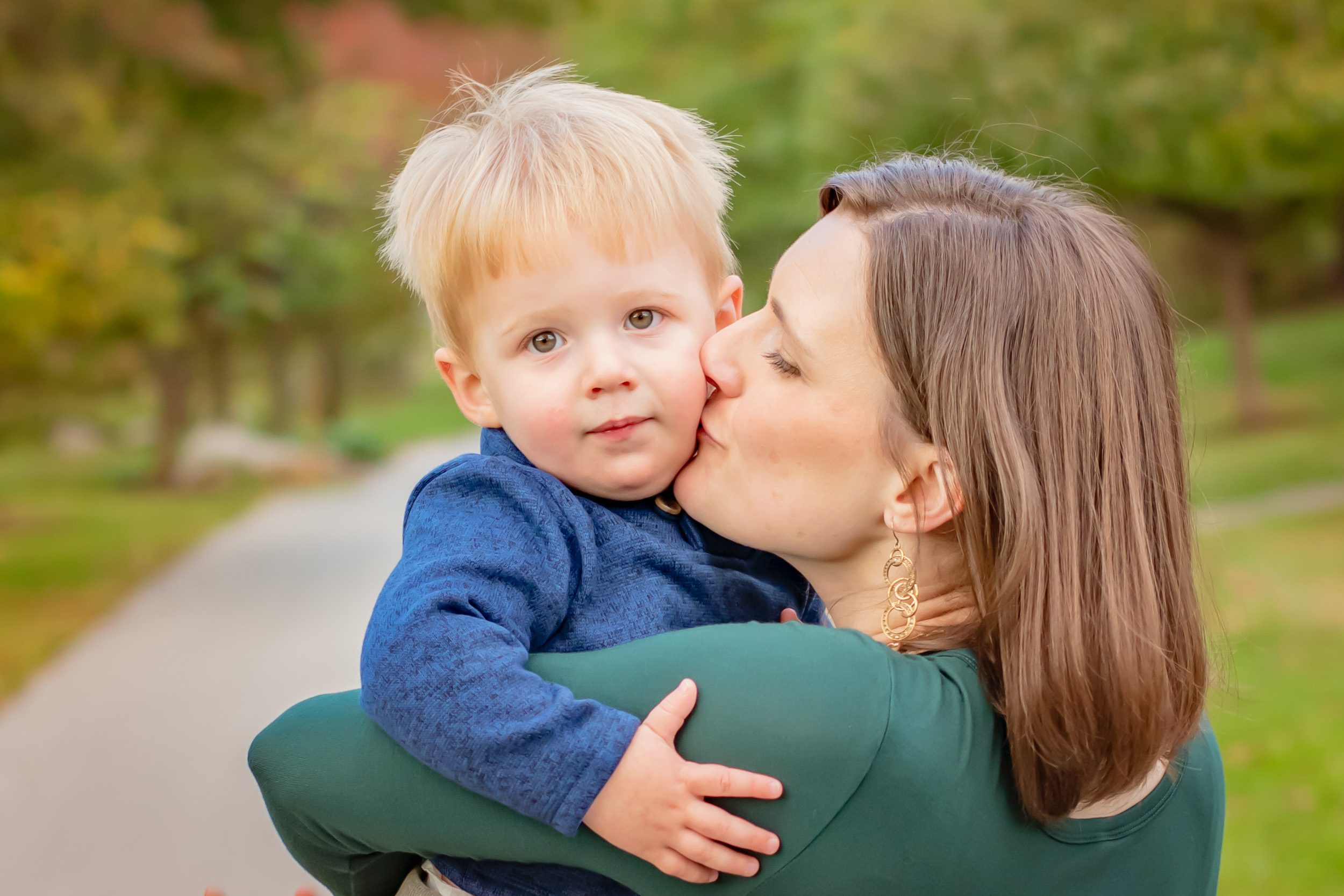 A young boy looking over his mom's shoulder as she kisses him on the cheek during a family photoshoot