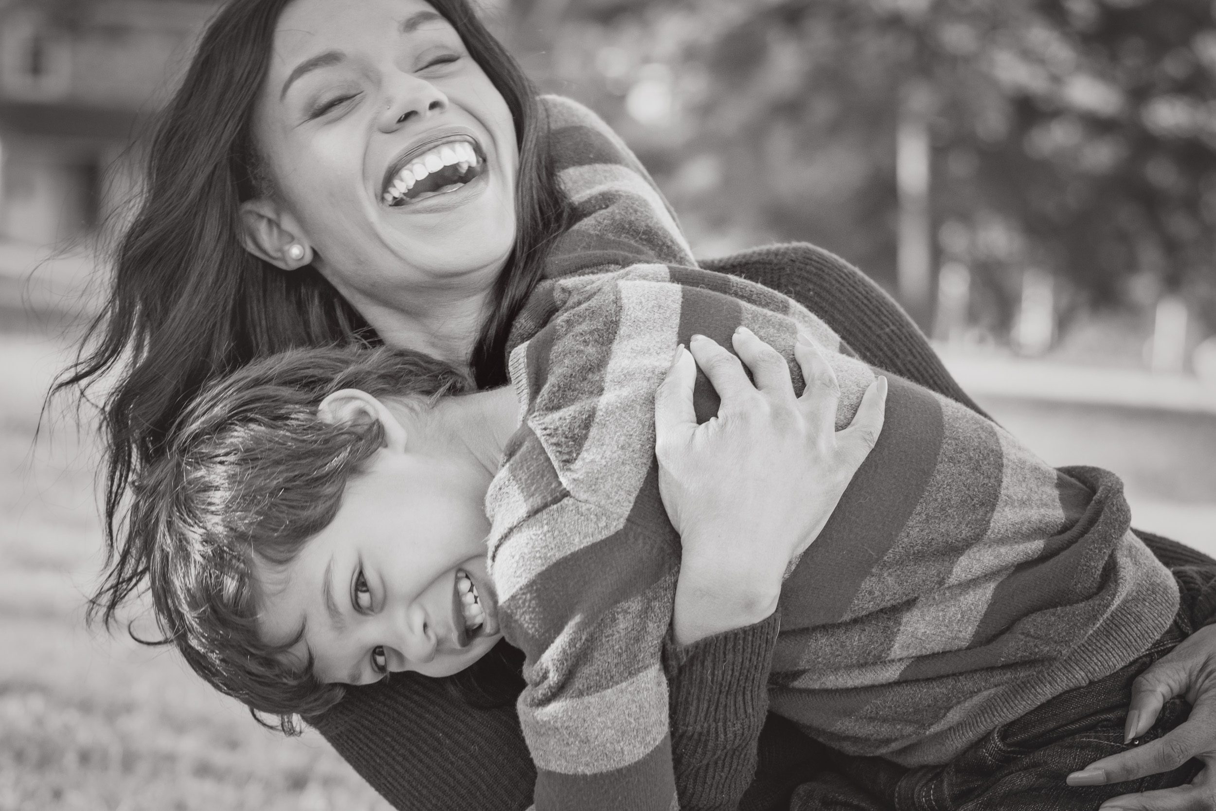 Black and white photo of a little boy hugging his mom and looking back at the camera while she laughs during a family photo session
