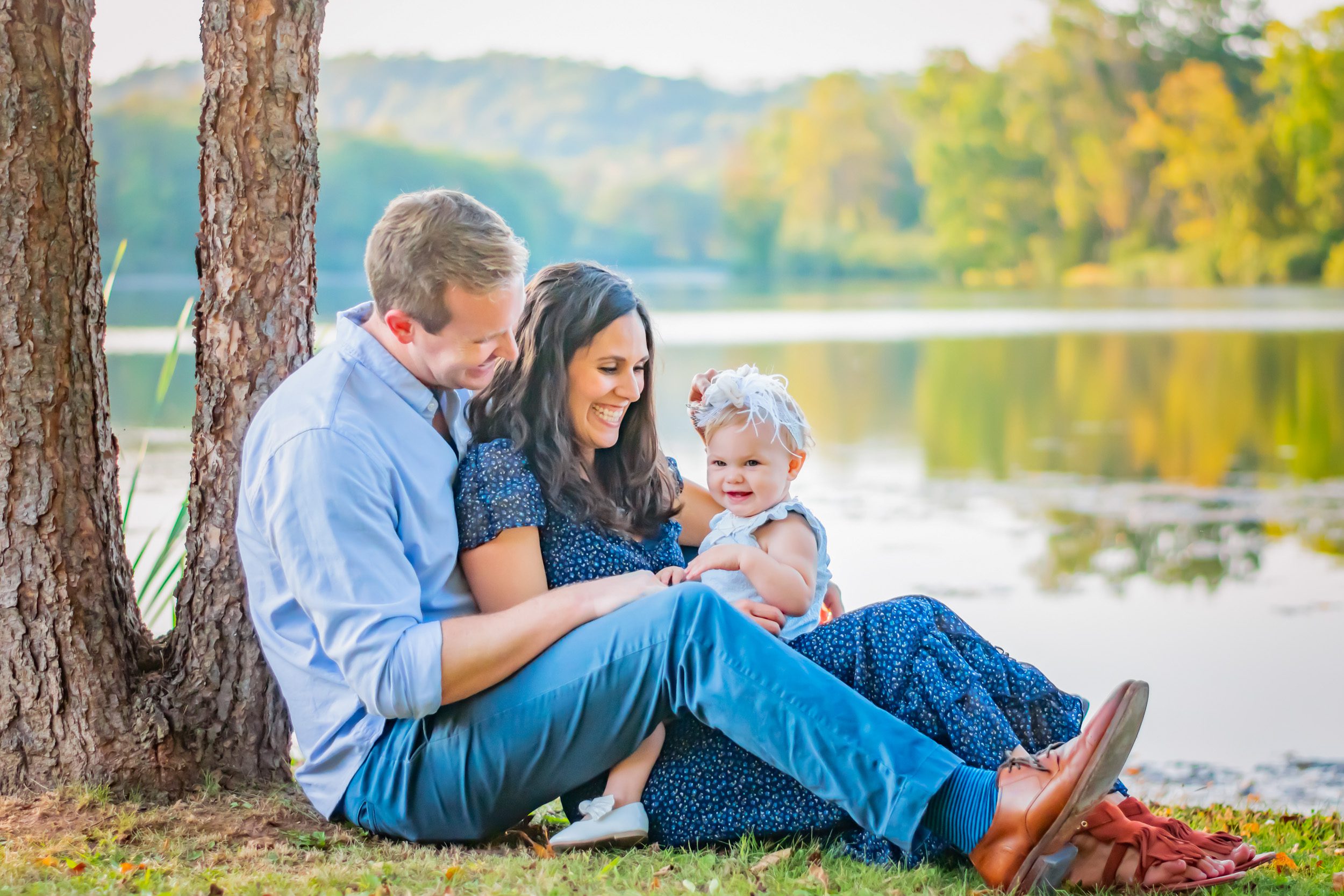 Family picture of parents sitting in front of a lake with their young daughter on their lap and laughing