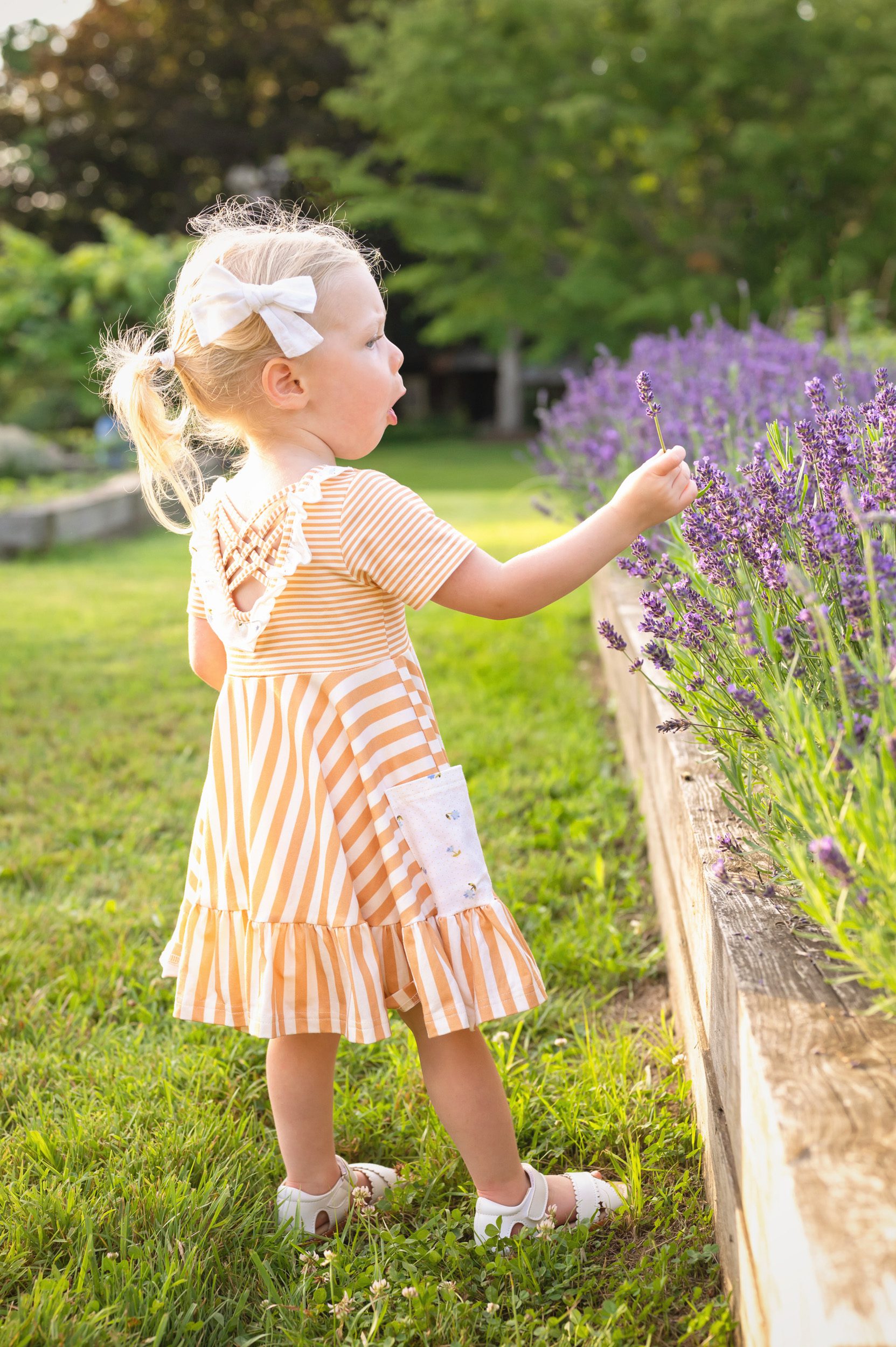 A young girl with an amazed expression reaching out to touch a lavender flower during a family photoshoot