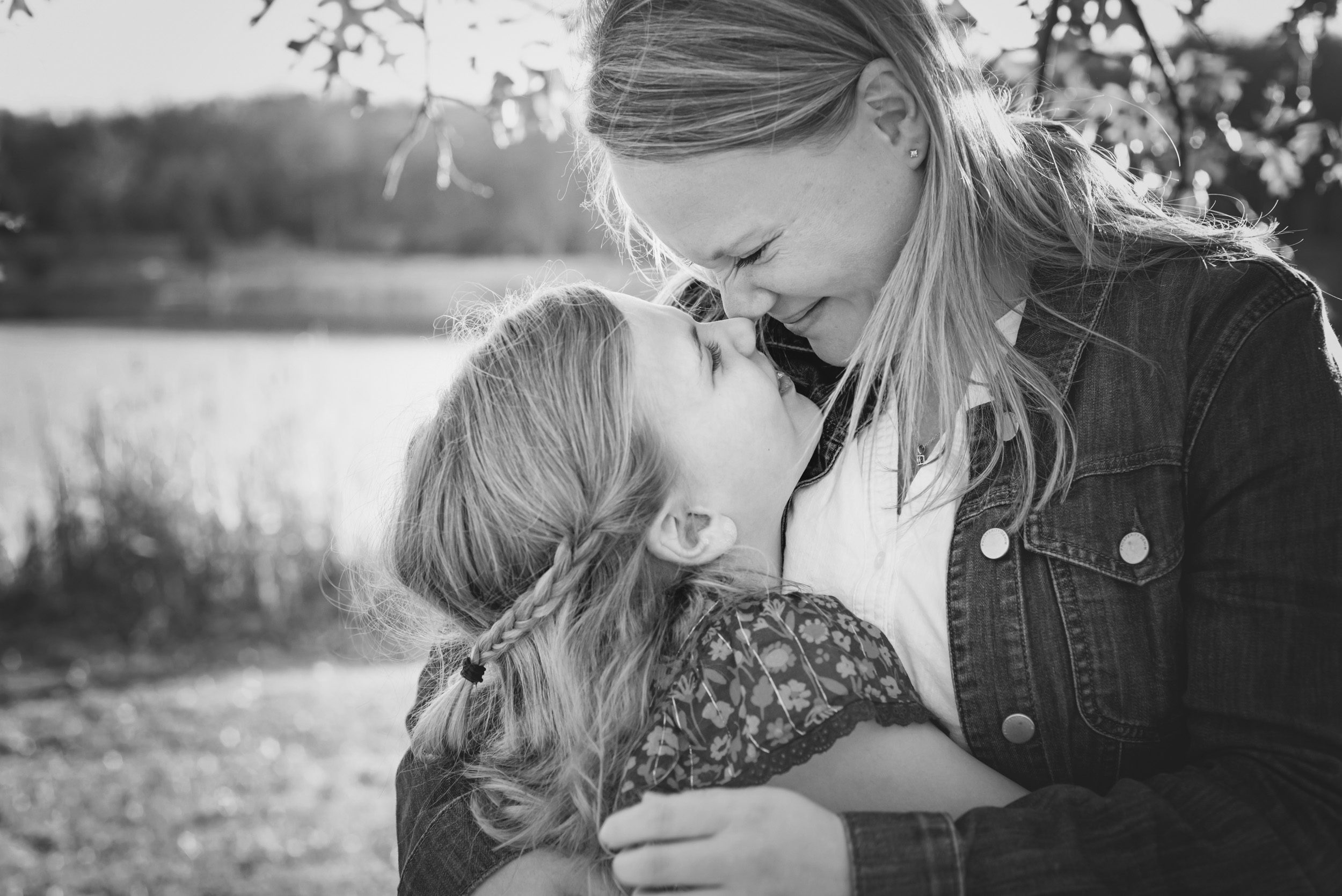 Black and white photo of a mom and her older daughter rubbing their noses together and smiling at each other during a family photo session