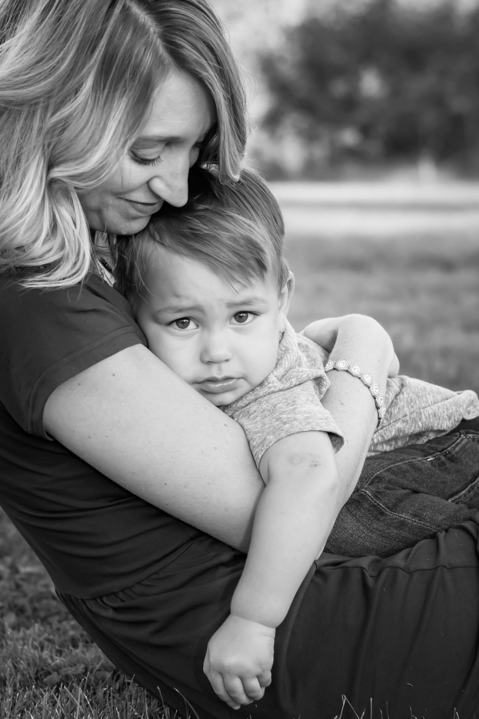 Black and white photo of a mom snuggling with her young son in the grass during a family photo session