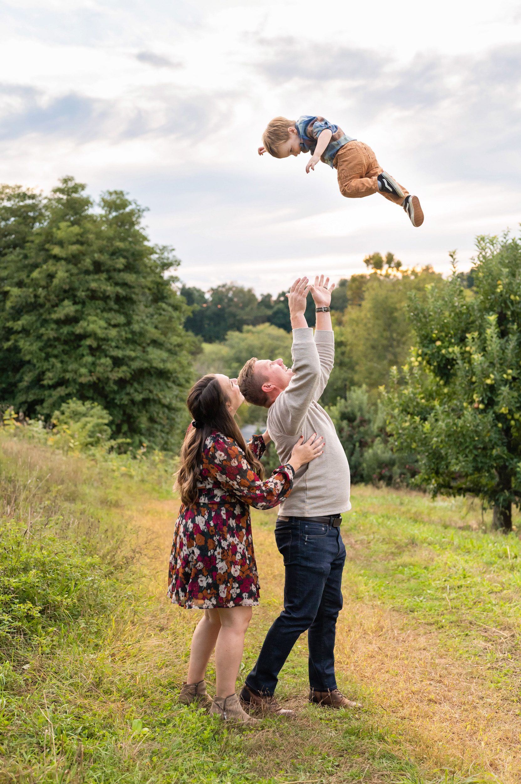 dad throwing his young son high in the air while mom hugs dad from behind during a family photoshoot