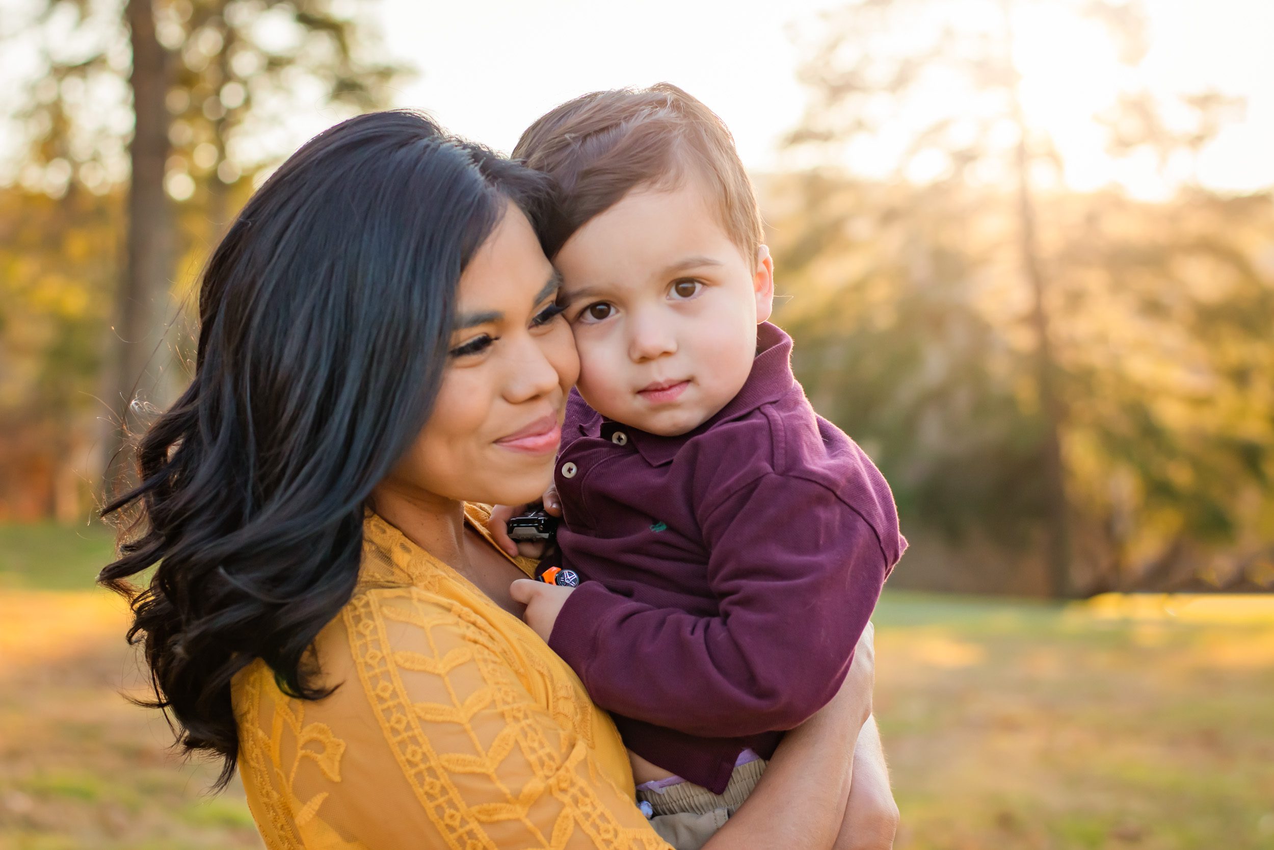 A little boy gazes at the camera as he rests his cheek against his mom during a family photo session