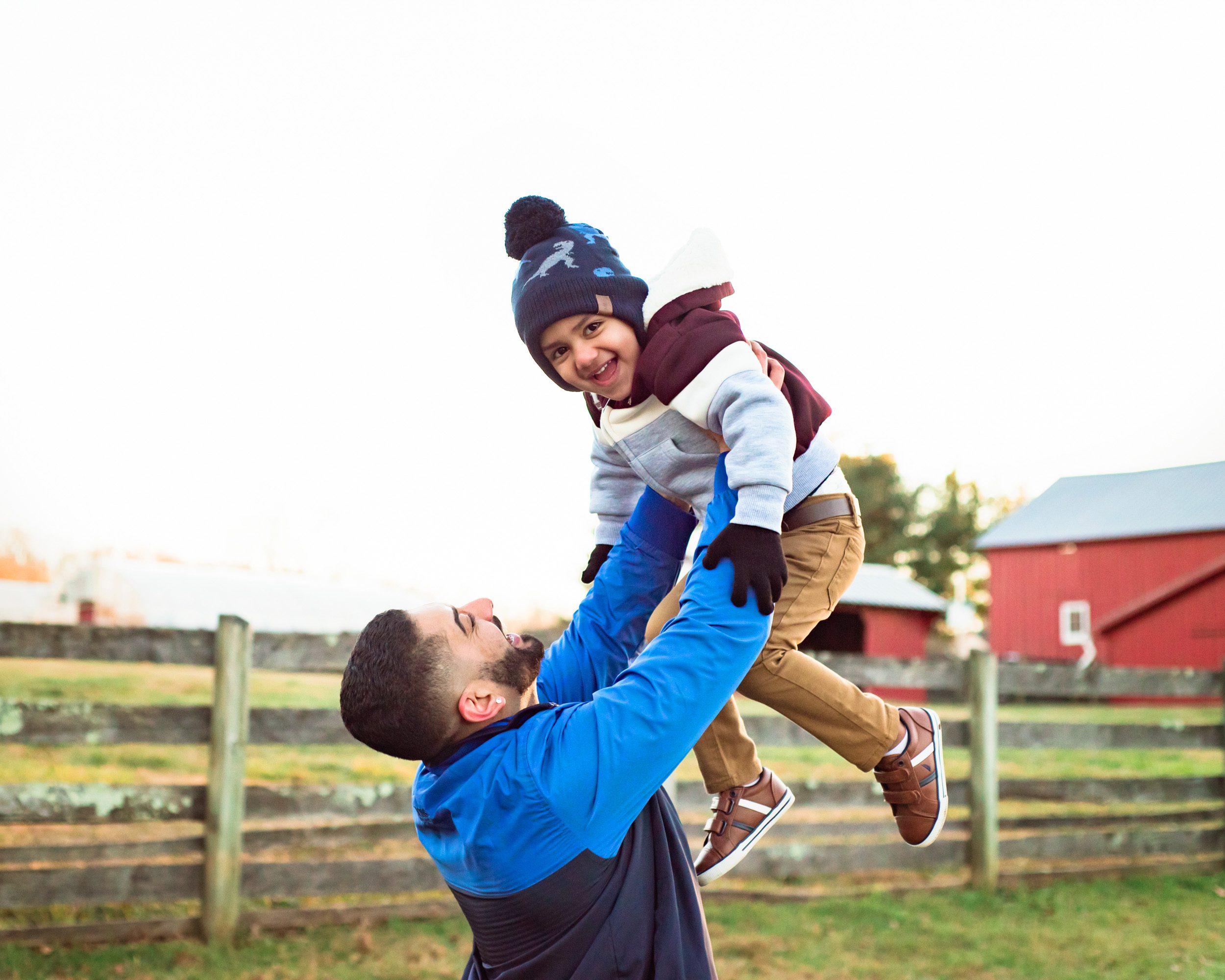 A young boy looking at the camera and smiling as his dad holds him high up in the air above his head during a family photo session