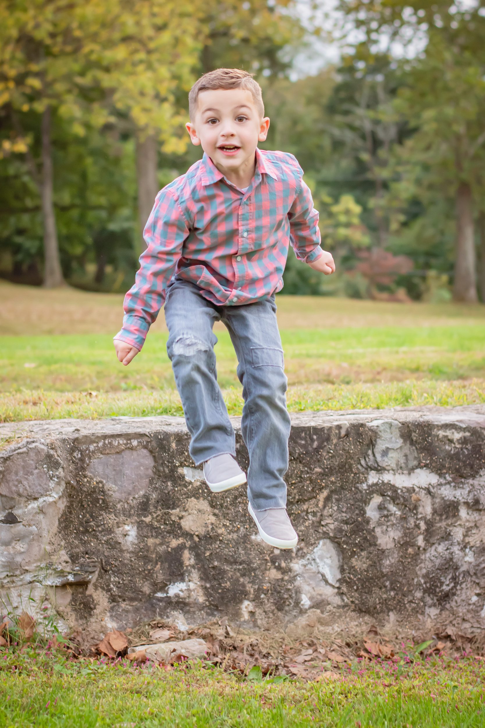 A young boy jumping off a stone wall and staring intently at the camera during a family photoshoot