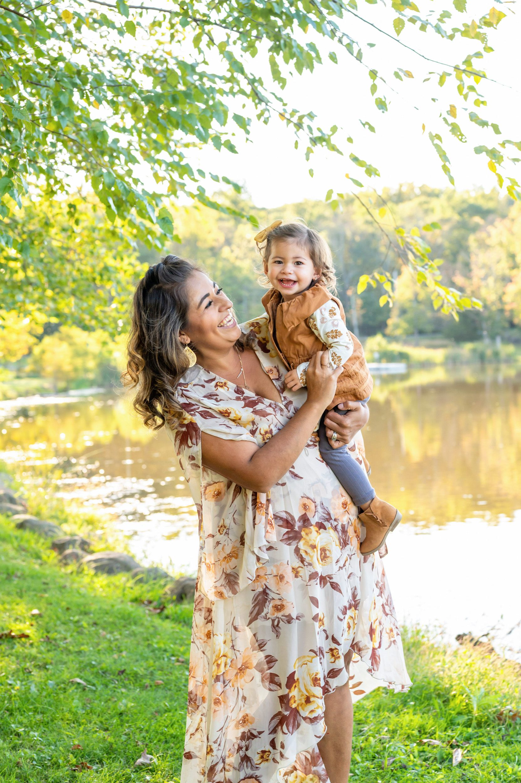 A mom holding her young daughter in front of a lake during a family photo session