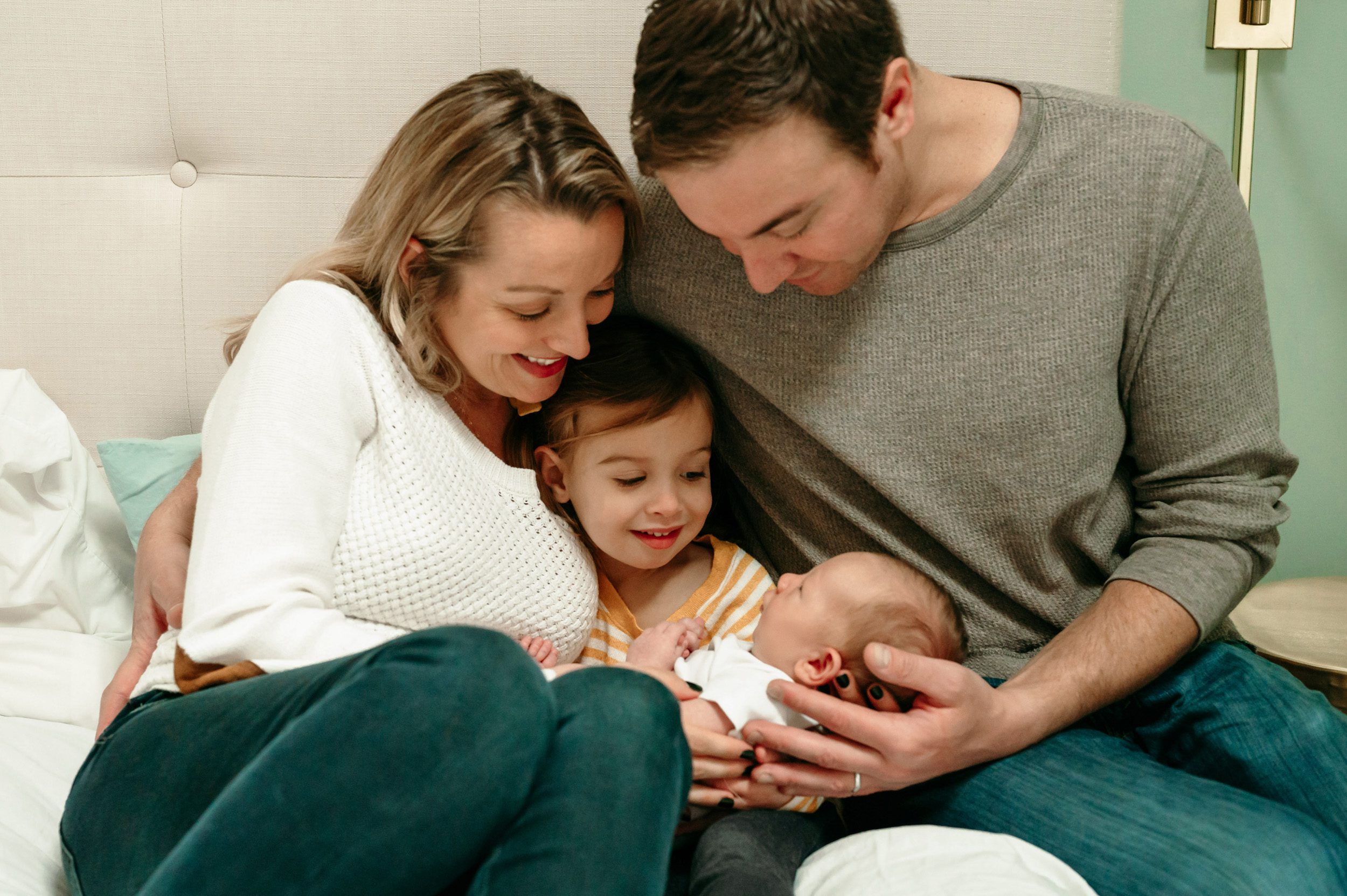 family of four snuggling with their newborn baby boy on a bed during an in home newborn photoshoot
