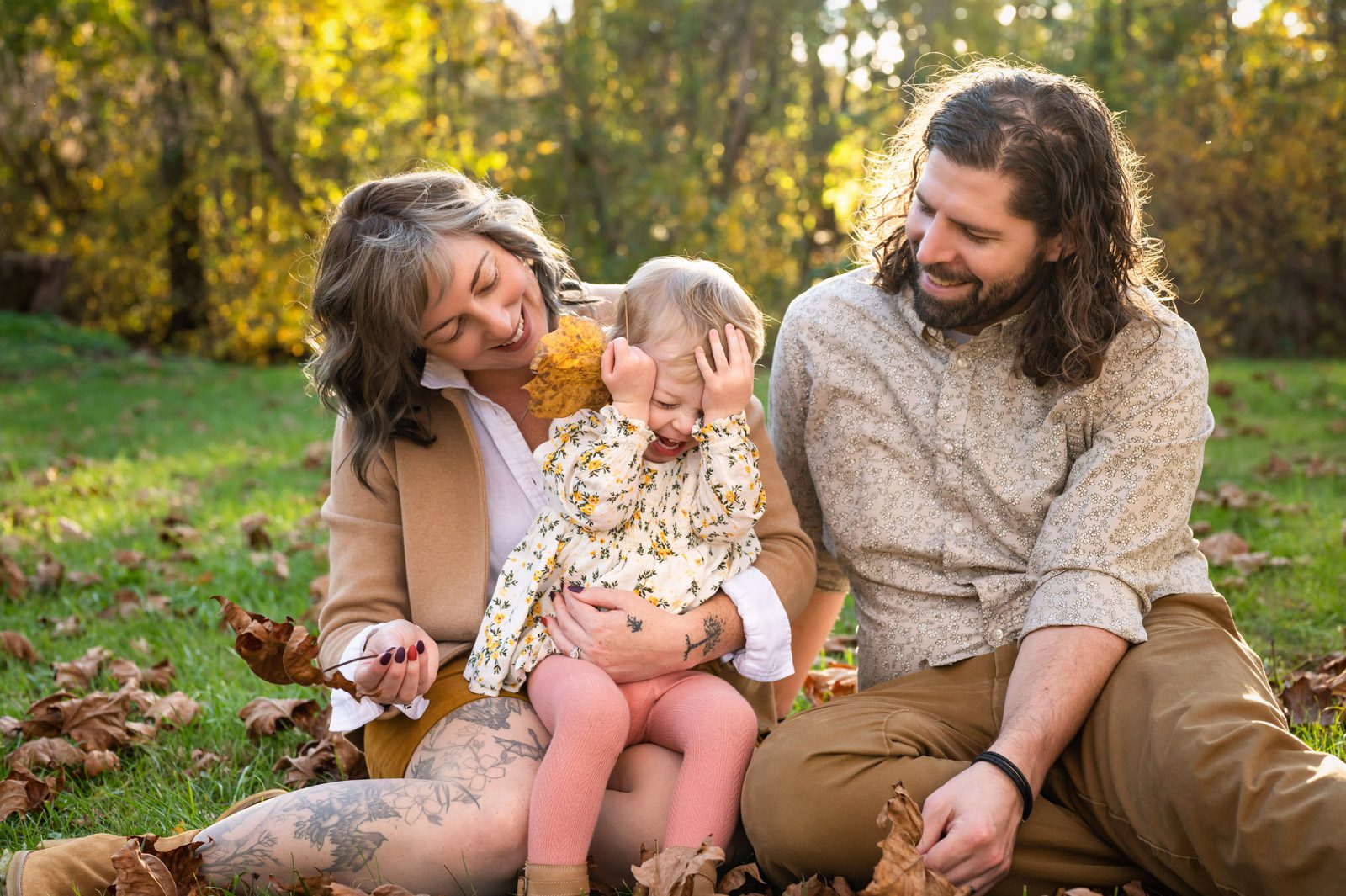 A young girl sitting on her parents lap and laughing as they smile down at her during a family photoshoot