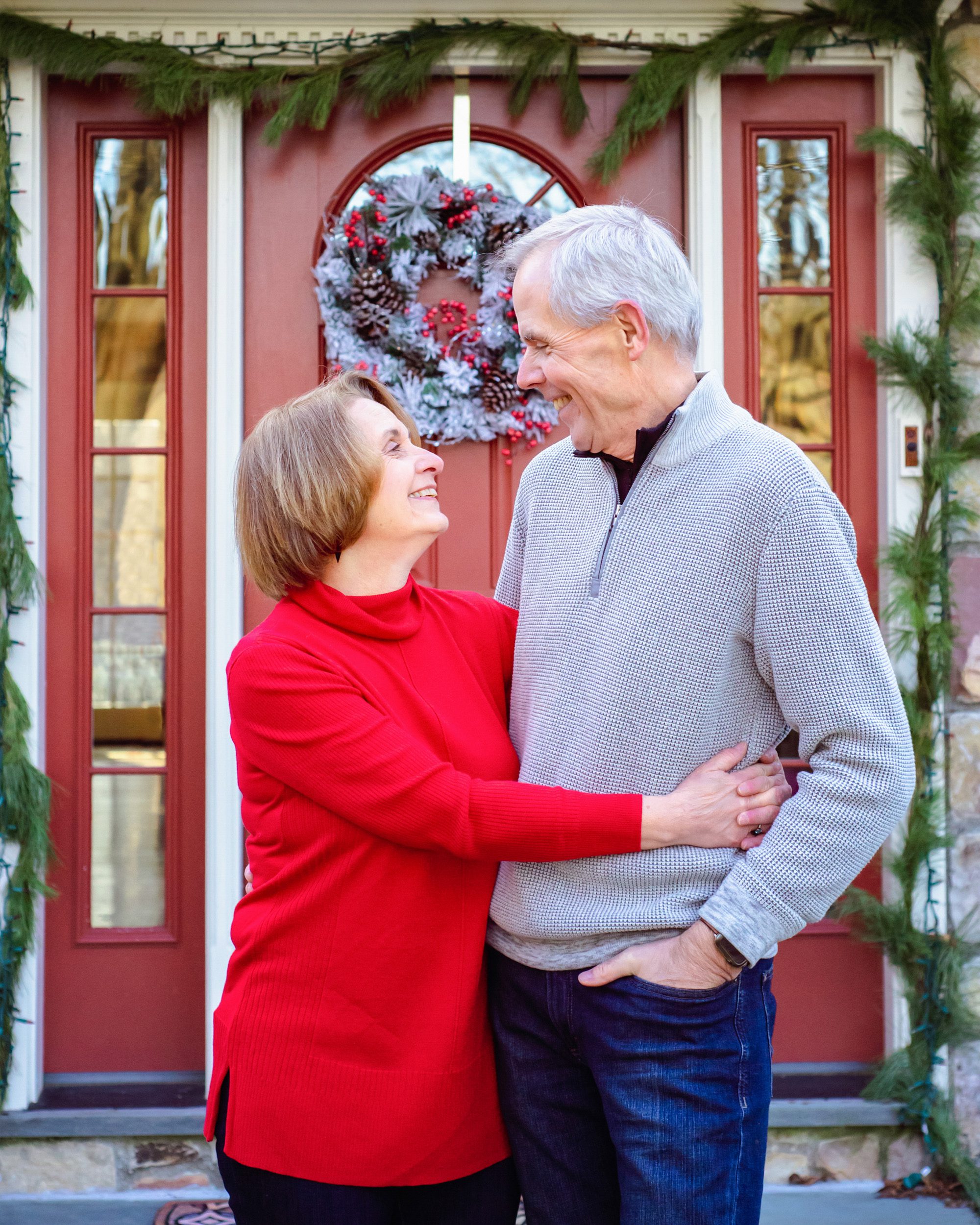 Grandparents standing in front of a red door hugging and smiling at each other during an extended family photoshoot