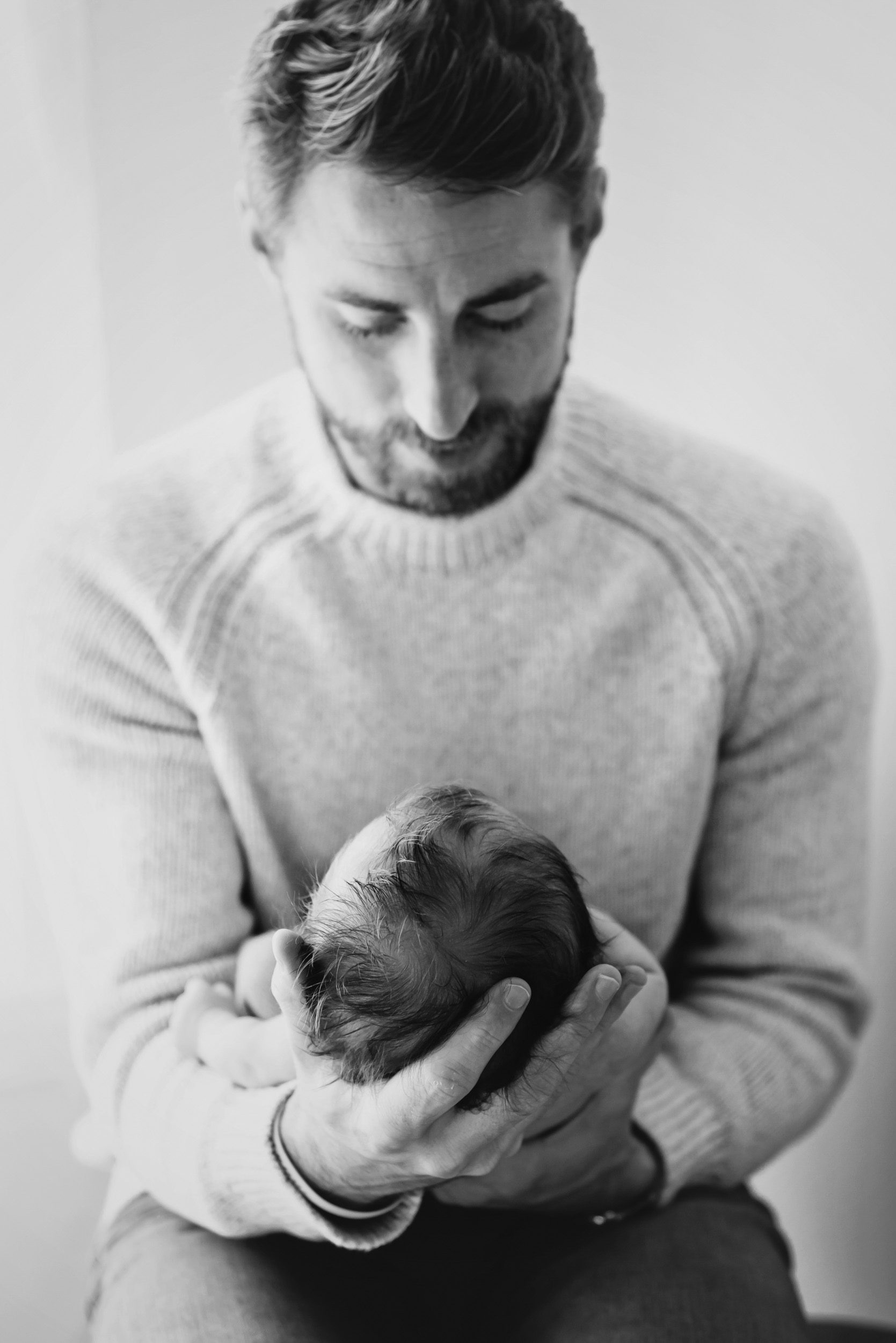black and white image of a new father gazing down at his newborn son in his arms during an in home newborn photoshoot