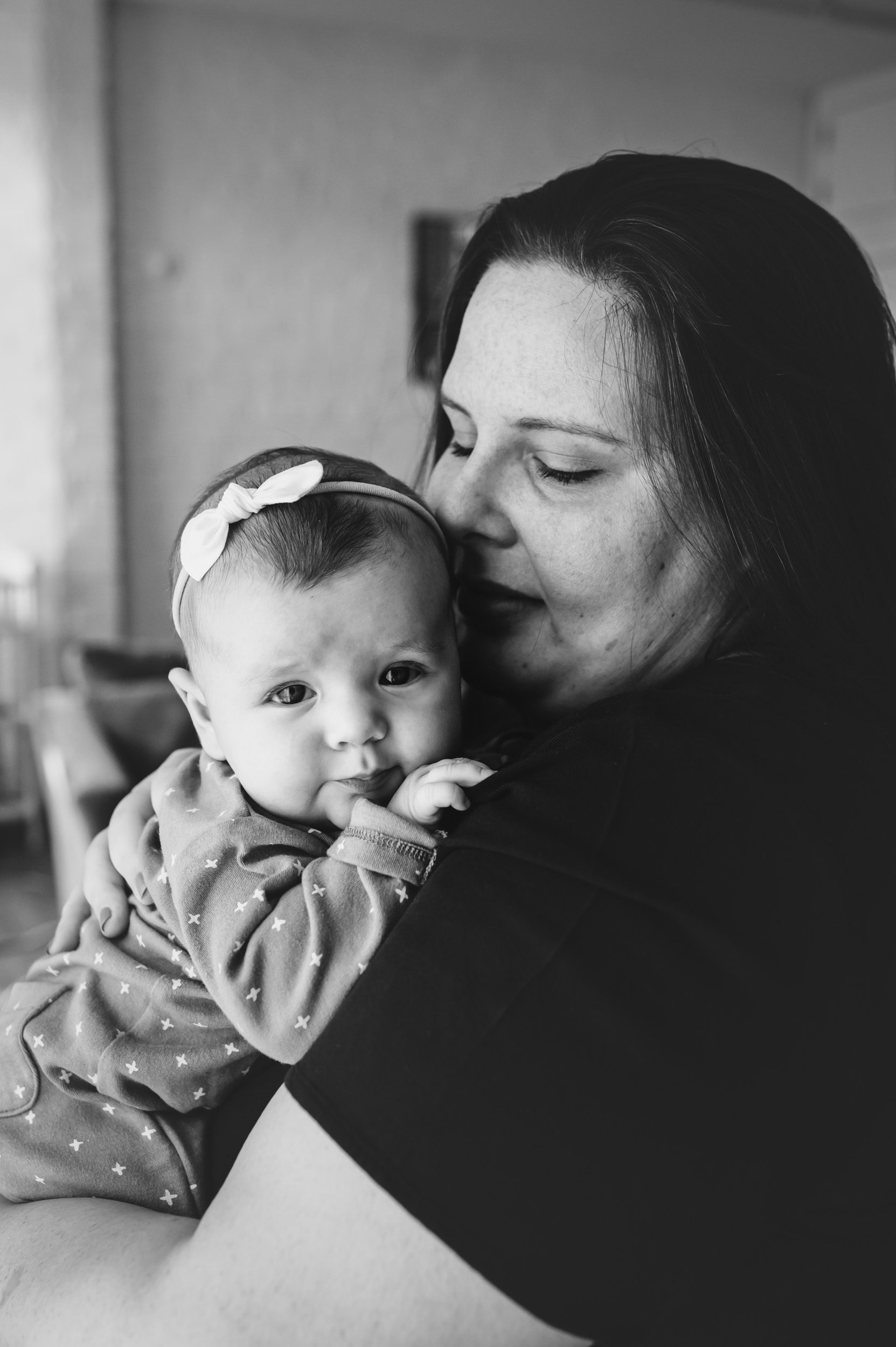Black and white image of a new mom snuggling her baby girl against her chest during a home newborn photo session