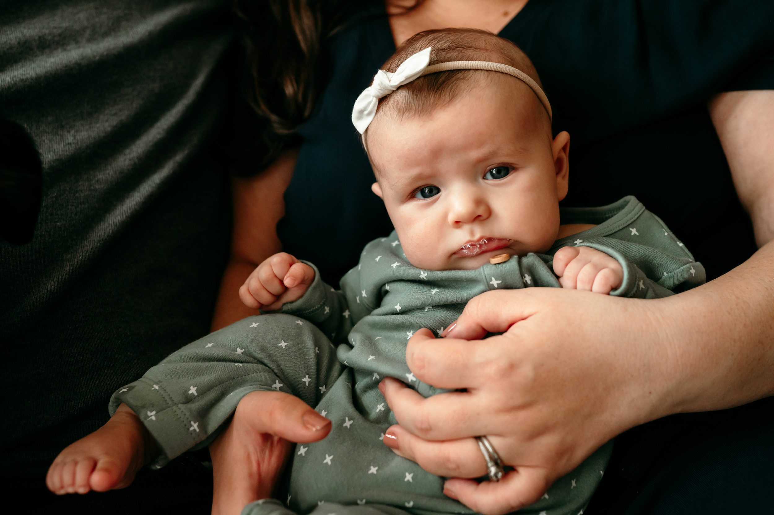 A close up of a baby girl in her mom's hands gazing at the camera blowing spit bubbles during a home newborn photo session