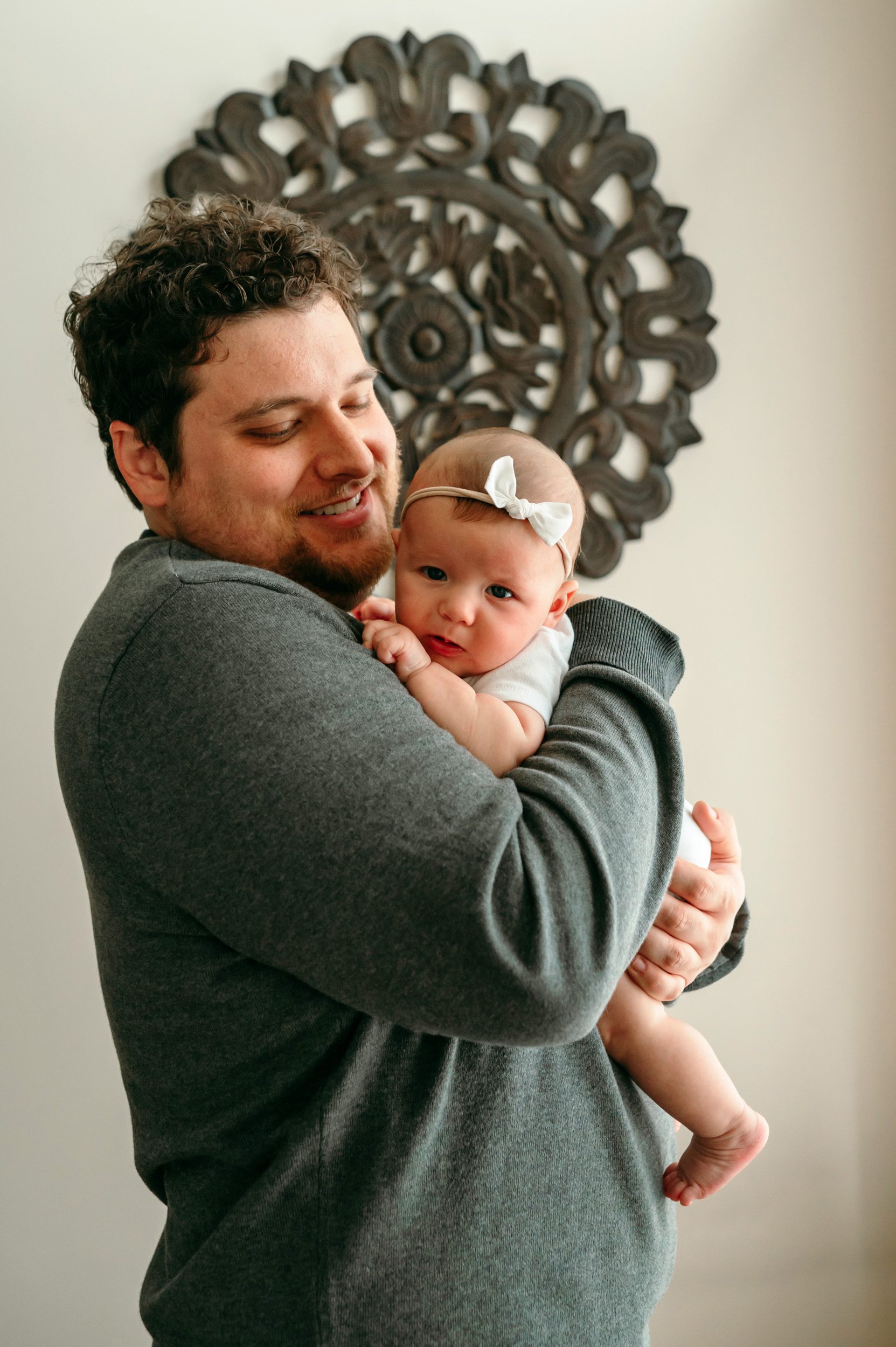 A new dad snuggling his newborn baby girl against his chest during a home newborn photoshoot