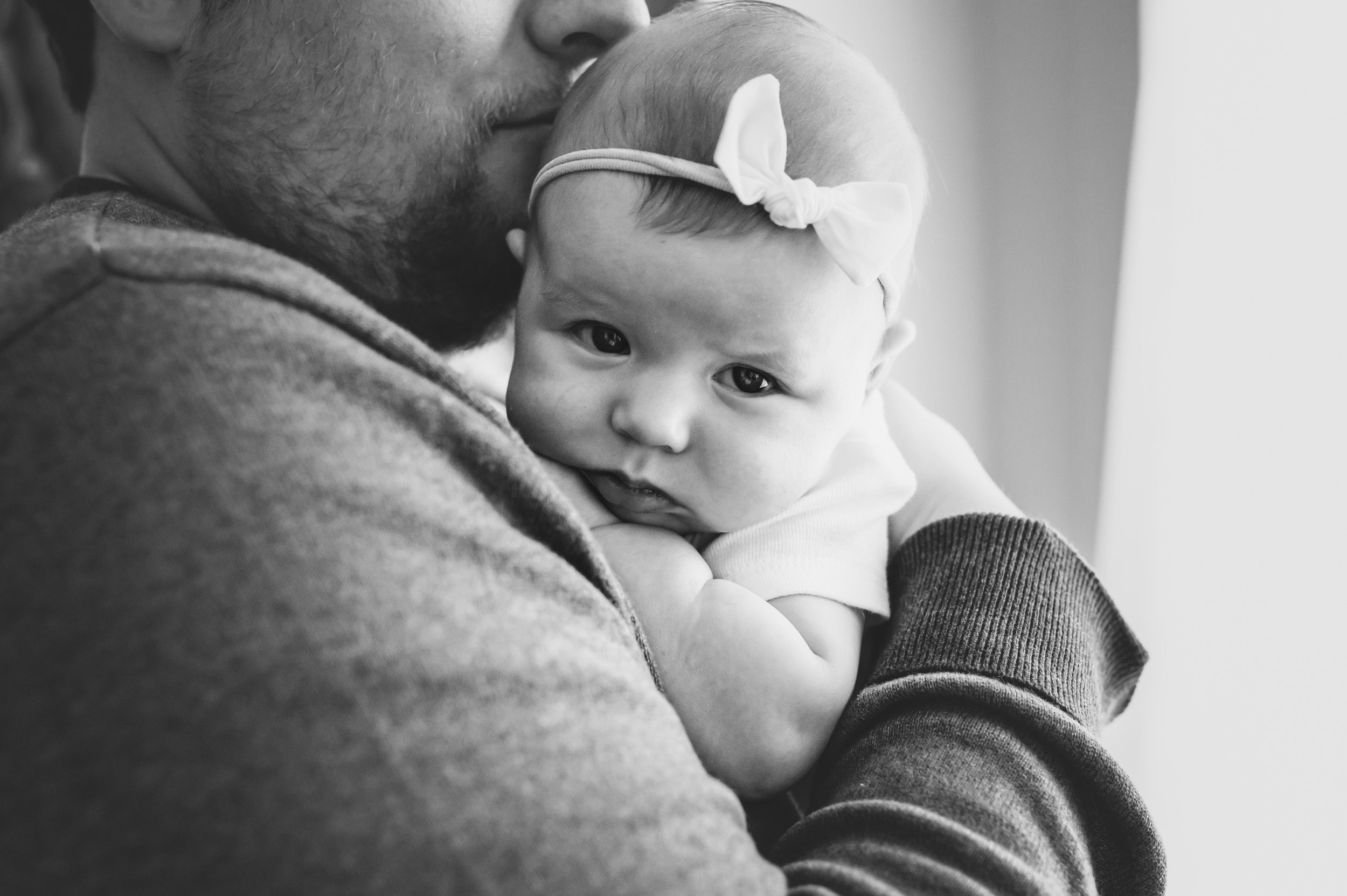 Black and white image of a dad kissing his baby girls temple at a home newborn photo session