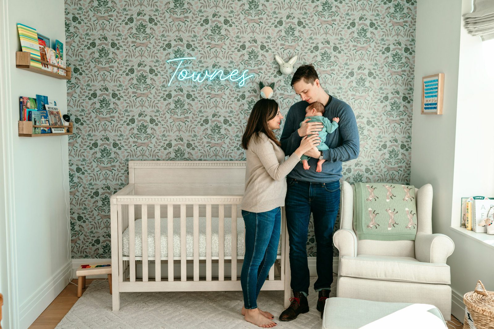 New parents standing in the nursery in front of the crib and holding their newborn son during a home newborn photoshoot