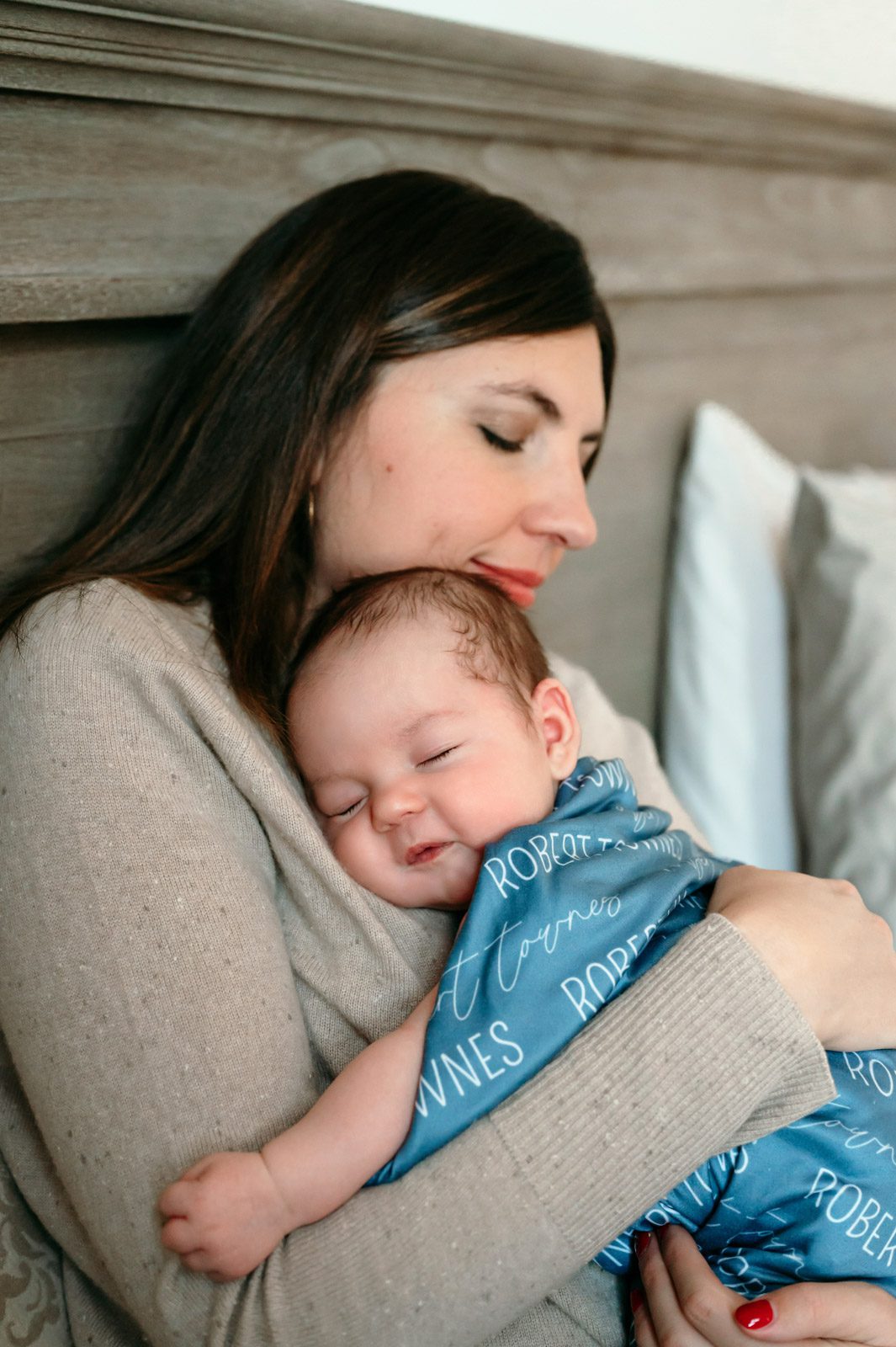 A new mom sitting on her bed snuggling her newborn baby boy against her chest during a home newborn photoshoot