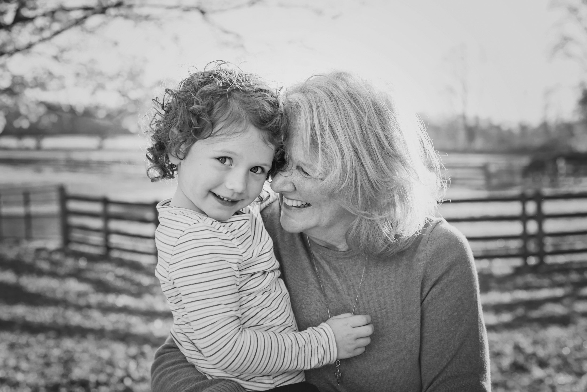 black and white image of a granddaughter smiling at the camera while her grandmother rests her nose against her cheek during an extended family photoshoot