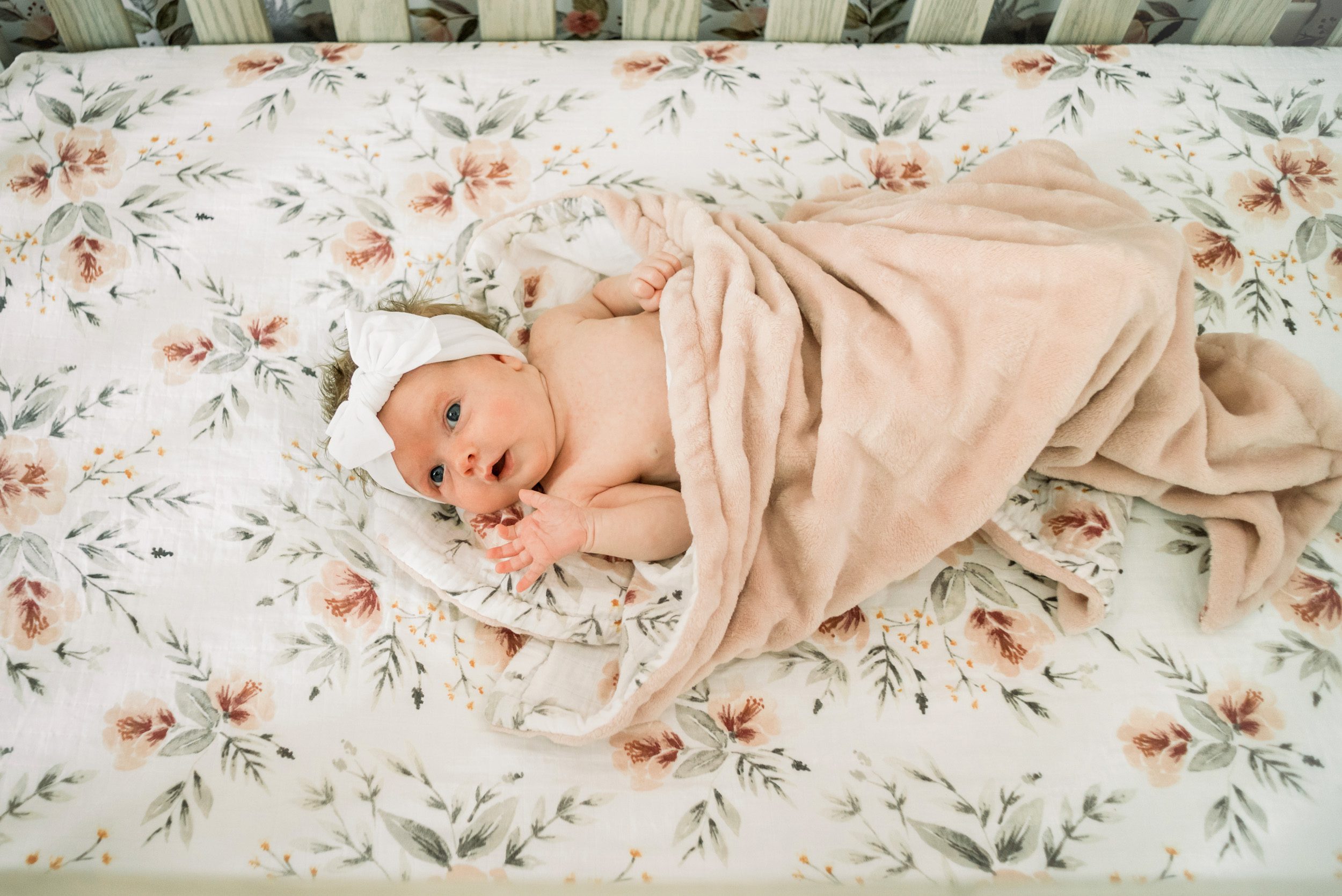 Newborn photo of baby girl laying in her crib looking up at her mom during an in home newborn photoshoot