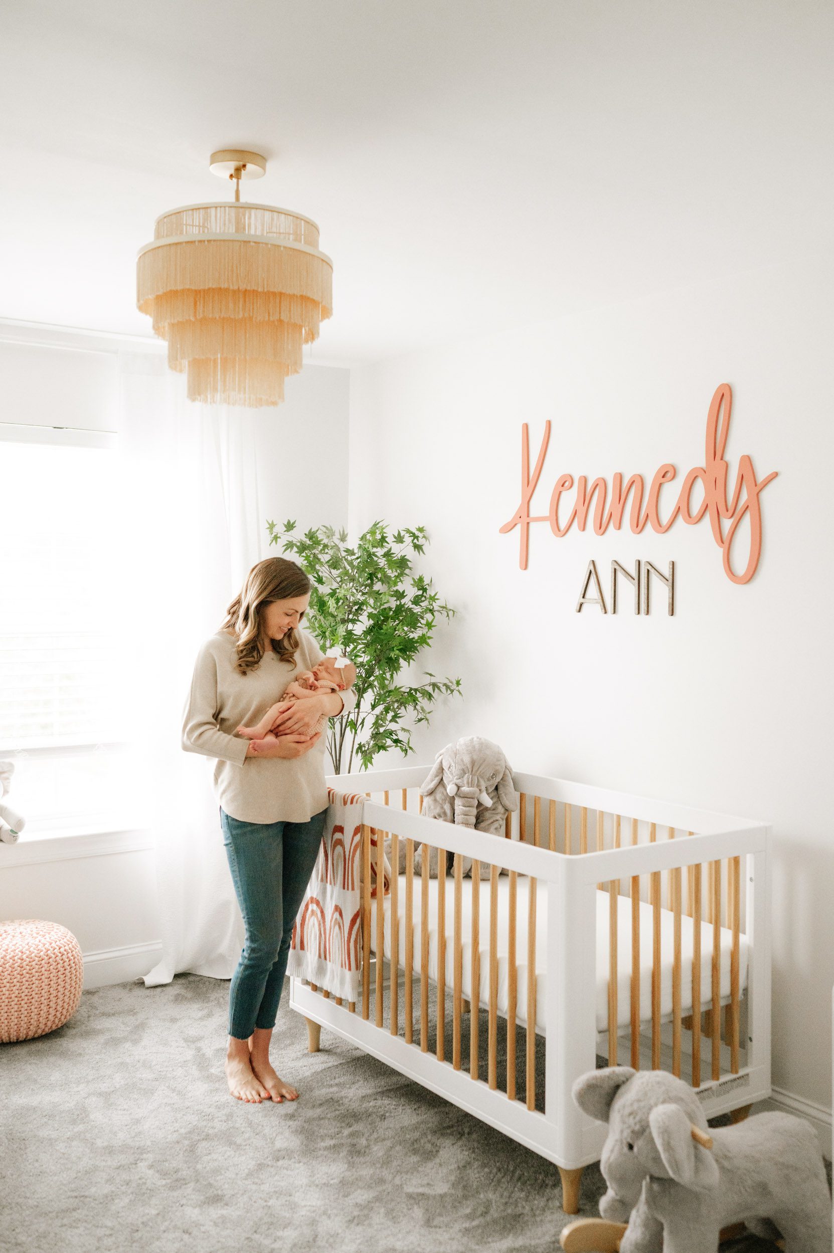 a new mom standing next to the crib in the nursery holding her baby girl in her arms and smiling down at her during a lifestyle newborn photoshoot