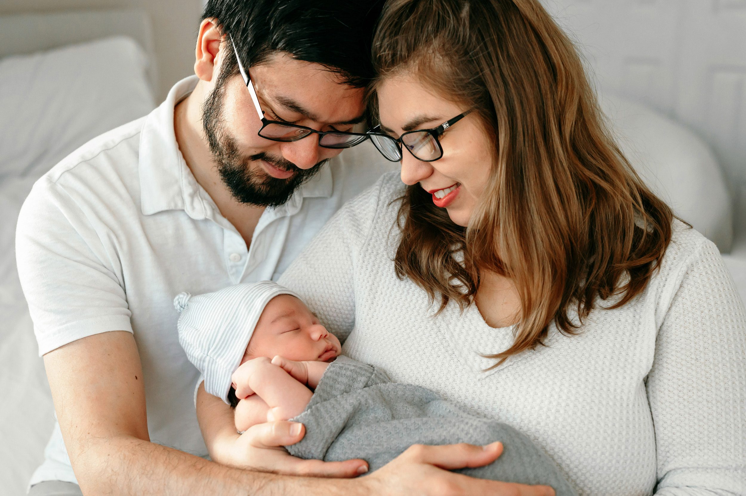 New parents holding their newborn baby boy and smiling down at him during a natural newborn photo session