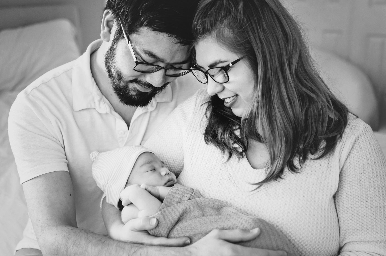 black and white image of new parents holding their newborn baby boy in their arms and smiling down at him during a reading newborn photoshoot